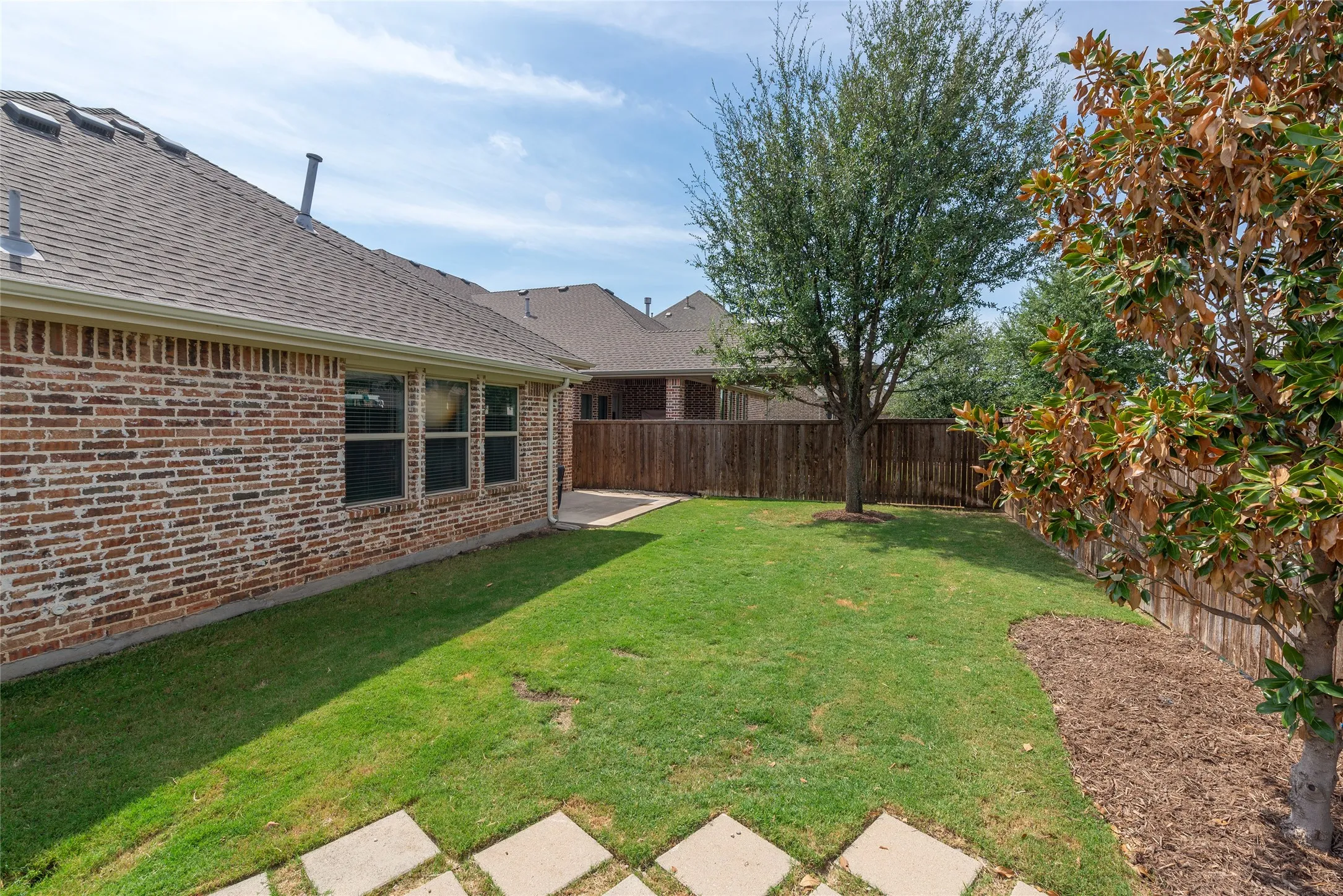 Expansive backyard featuring a manicured lawn, established trees, and a privacy fence