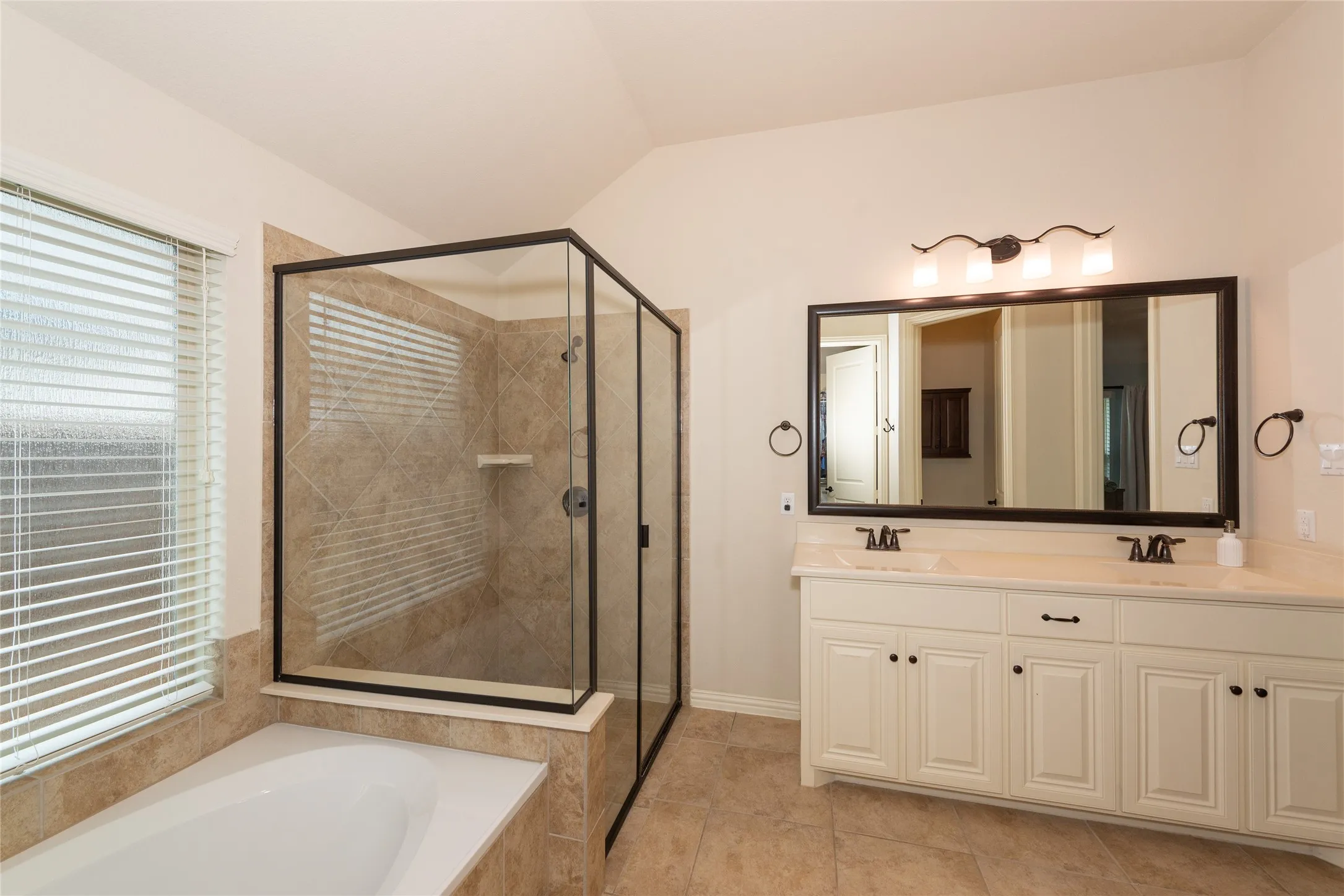 Tile flooring, dual vanity with undermount sinks, separate soaking tub, and enclosed shower with tile surround