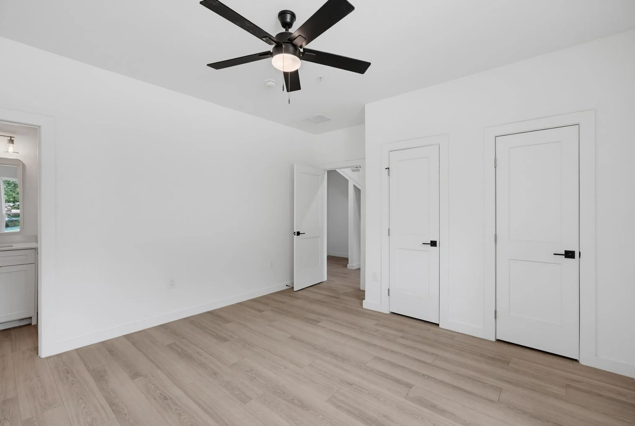 Light-toned wood-finish flooring, white walls, and a black ceiling fan with integrated lighting
