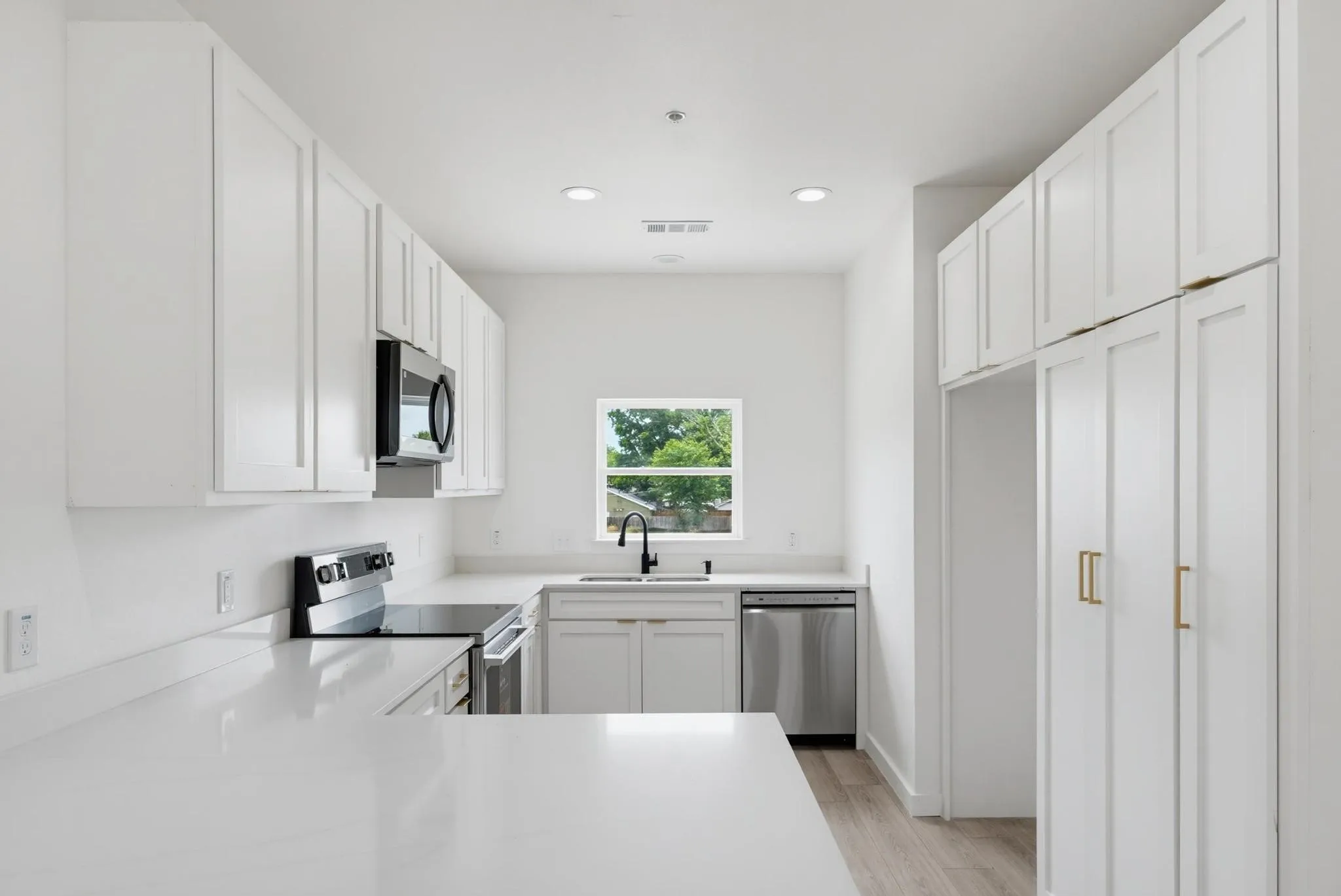 Kitchen featuring white shaker-style cabinetry, stainless steel appliances, white countertops, and wood-finish flooring
