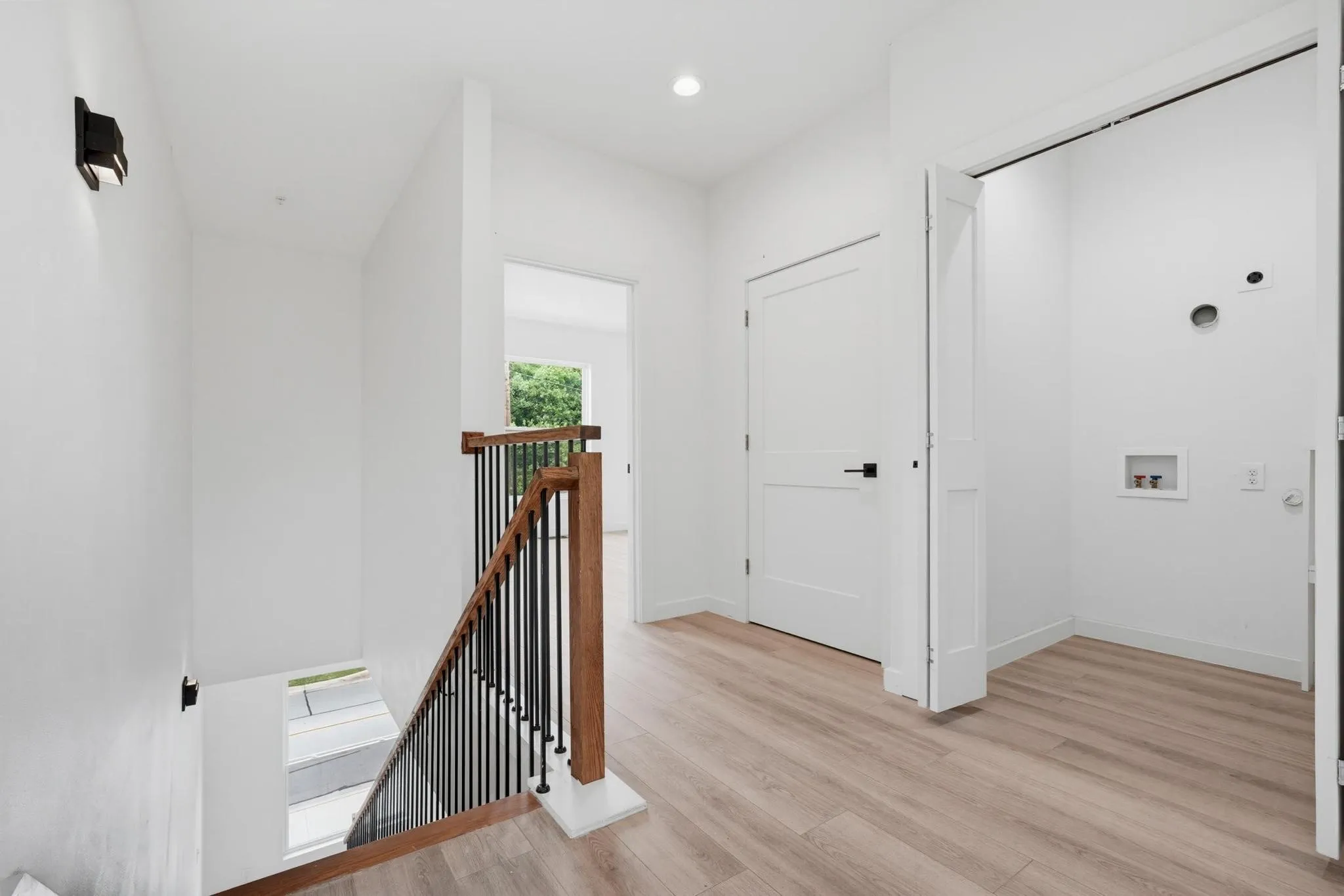 White walls, wood-finish flooring, staircase with wood handrail, black metal balusters, and a built-in laundry area