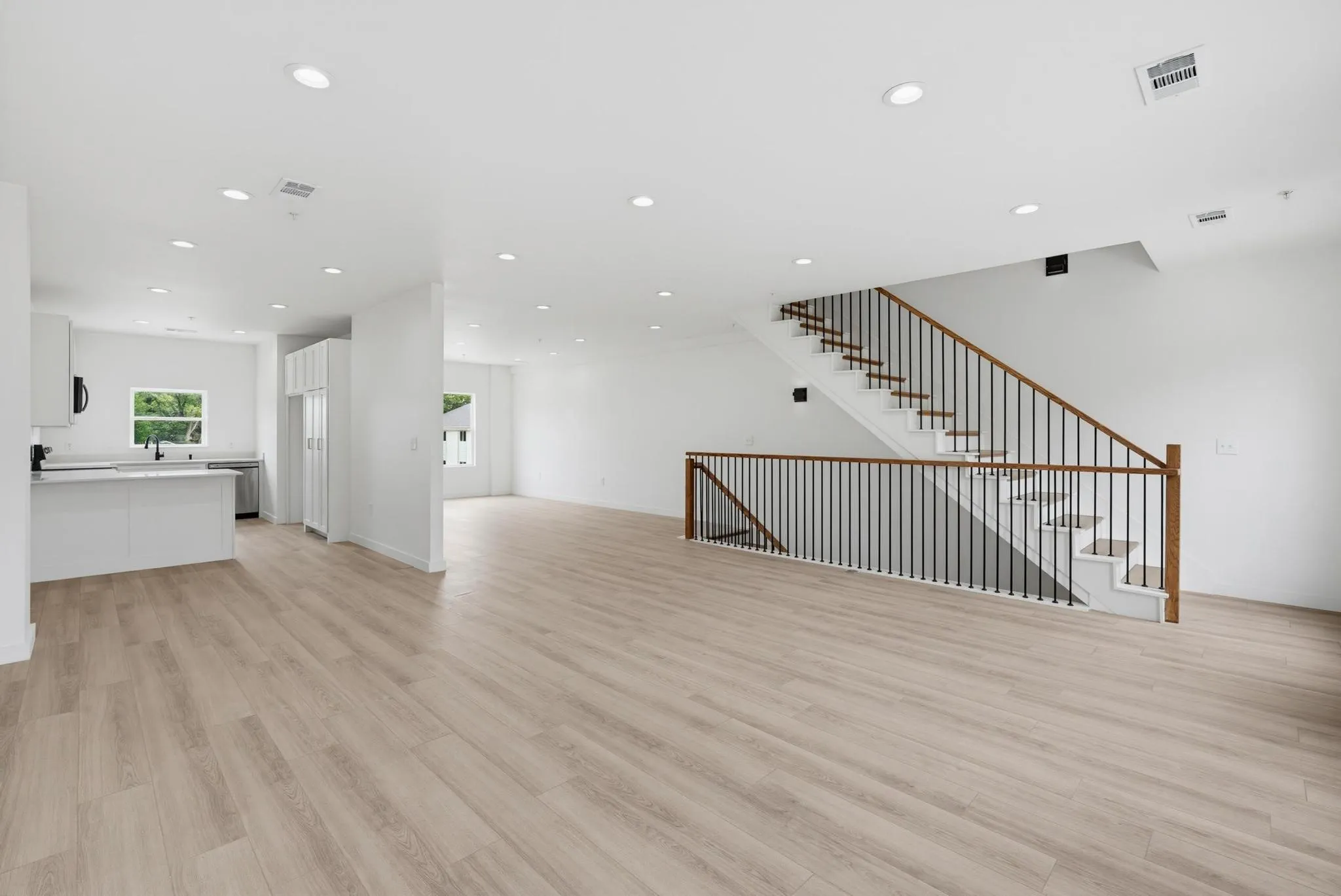 Open-concept living area featuring light wood-finish flooring, recessed lighting, and a modern staircase with dark balusters and wood handrails