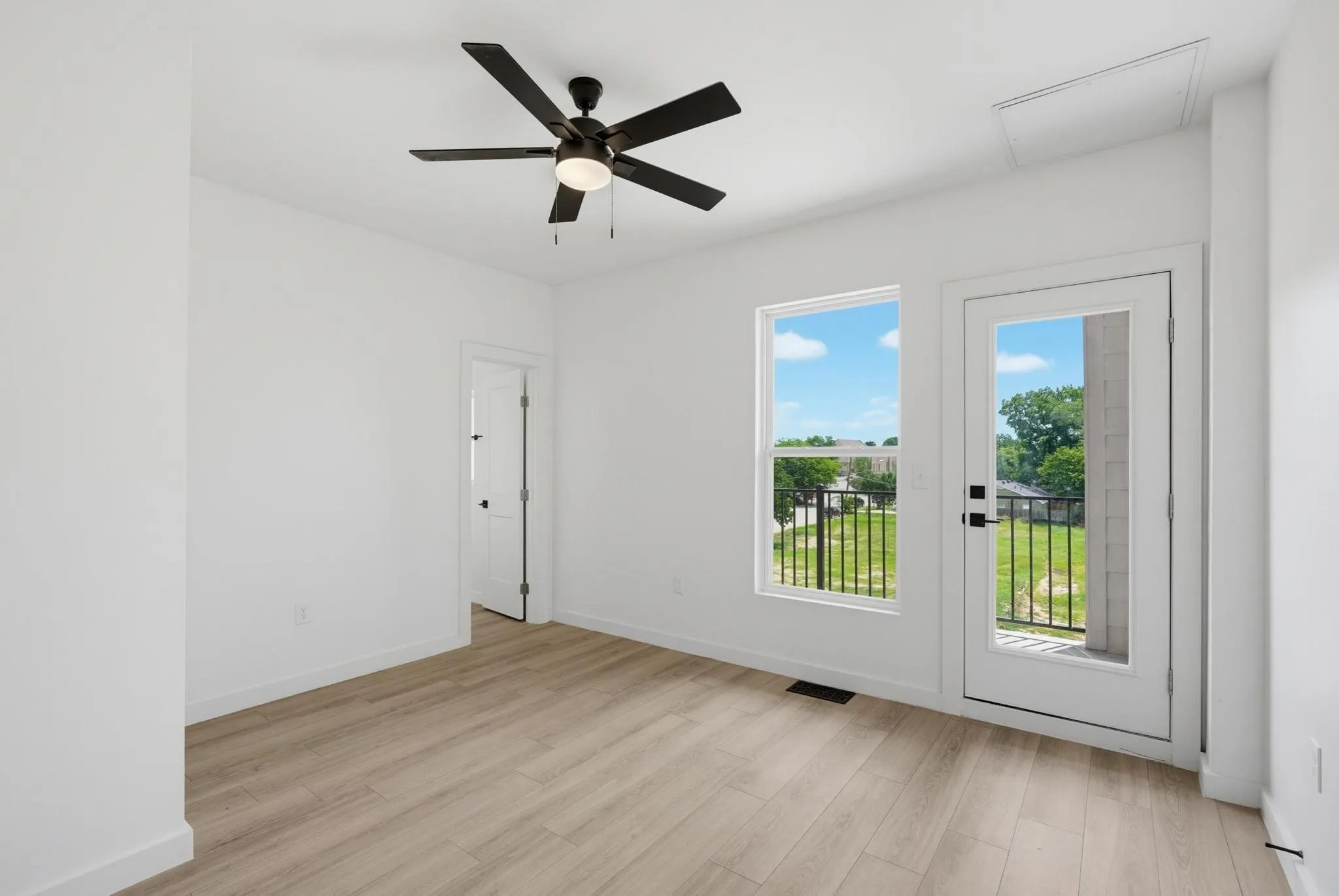 Wood-finish flooring, white walls, and a black ceiling fan with integrated lighting