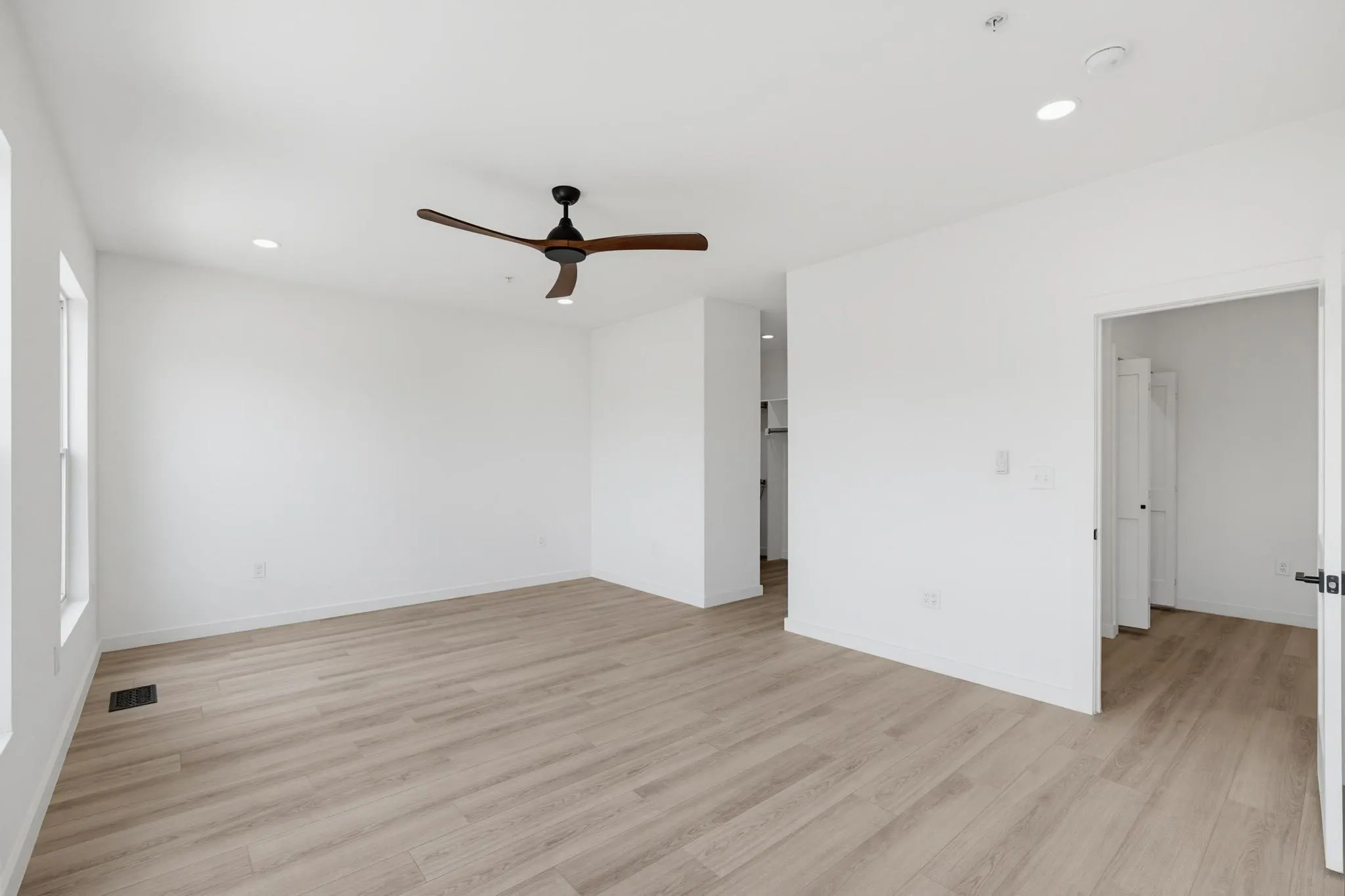 Spacious room with light wood-finish flooring, recessed lighting, and a modern ceiling fan