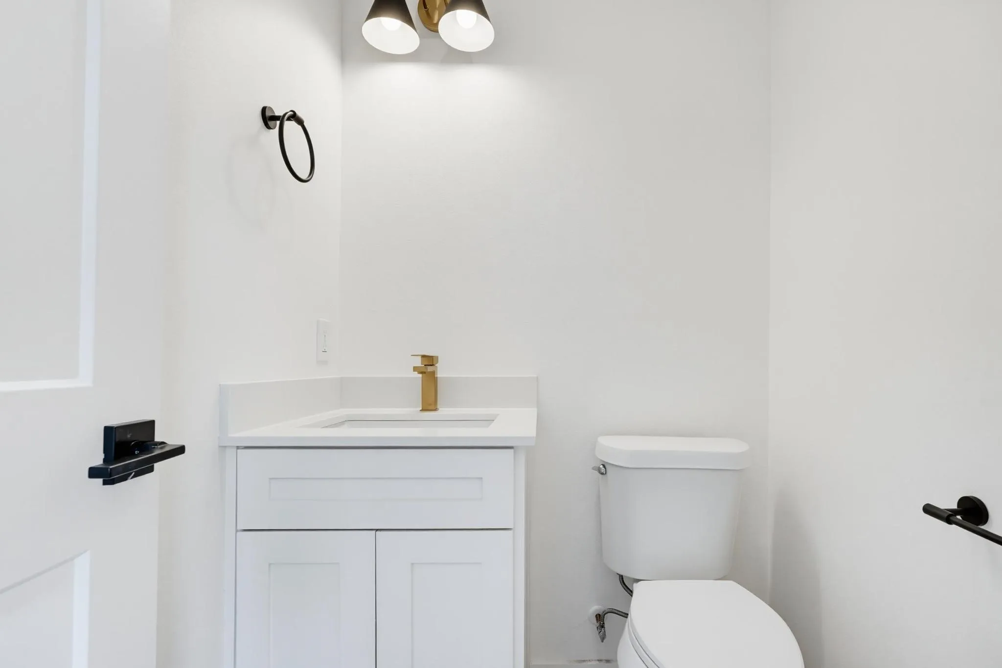 White shaker-style vanity with a single basin and gold-finish faucet, white countertop, and wall-mounted light fixture