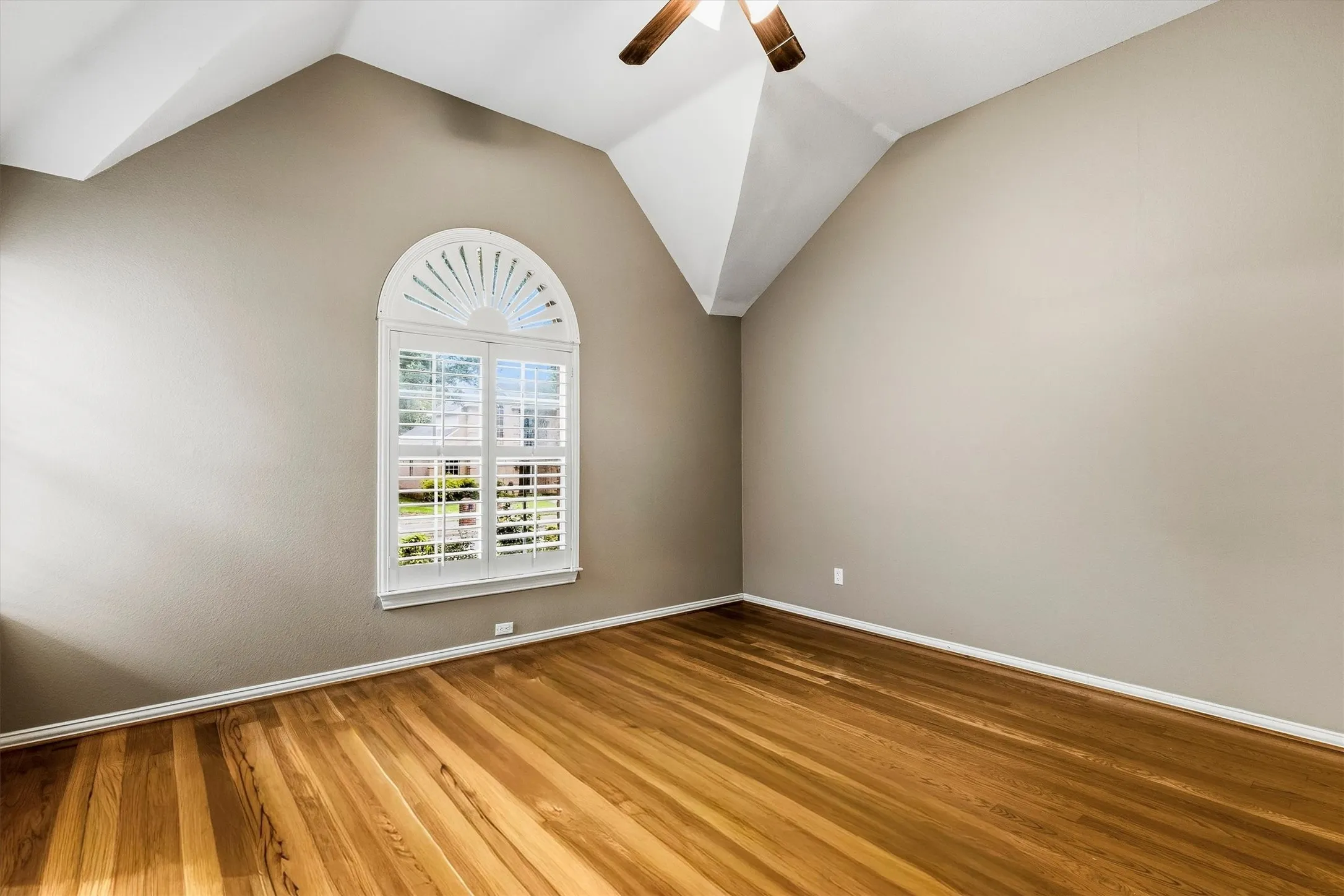 Wood-finish flooring, vaulted ceiling, arched window with plantation shutters, ceiling fan