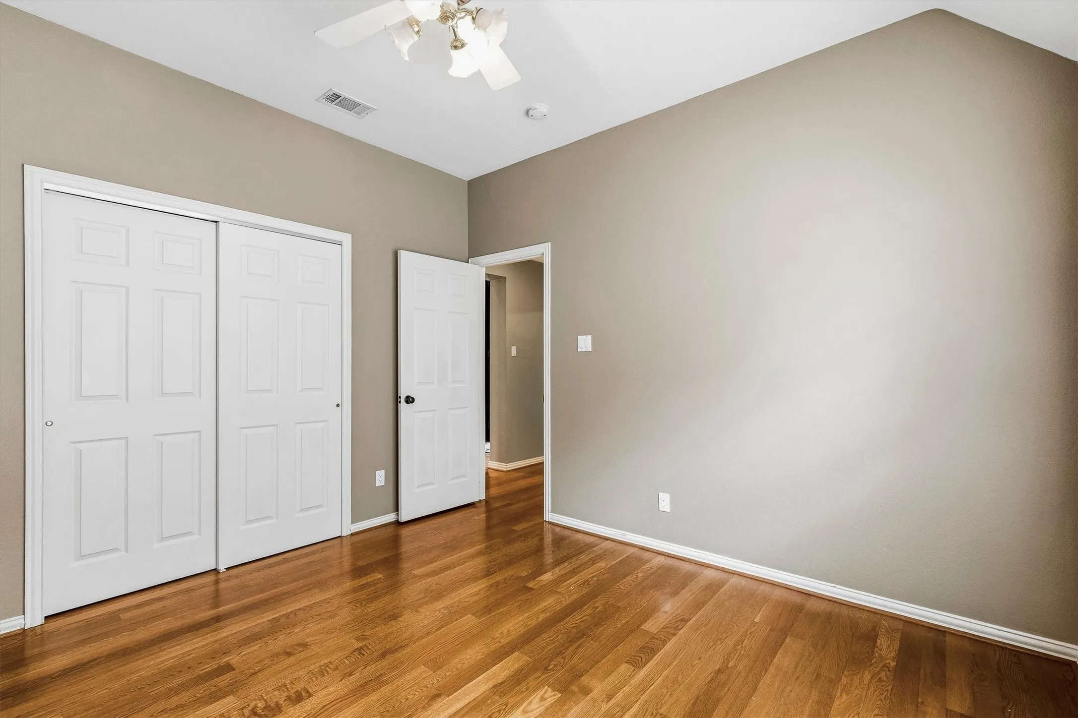 Wood-finish flooring, vaulted ceiling, ceiling fan with integrated lighting, two-panel closet doors, and neutral wall paint