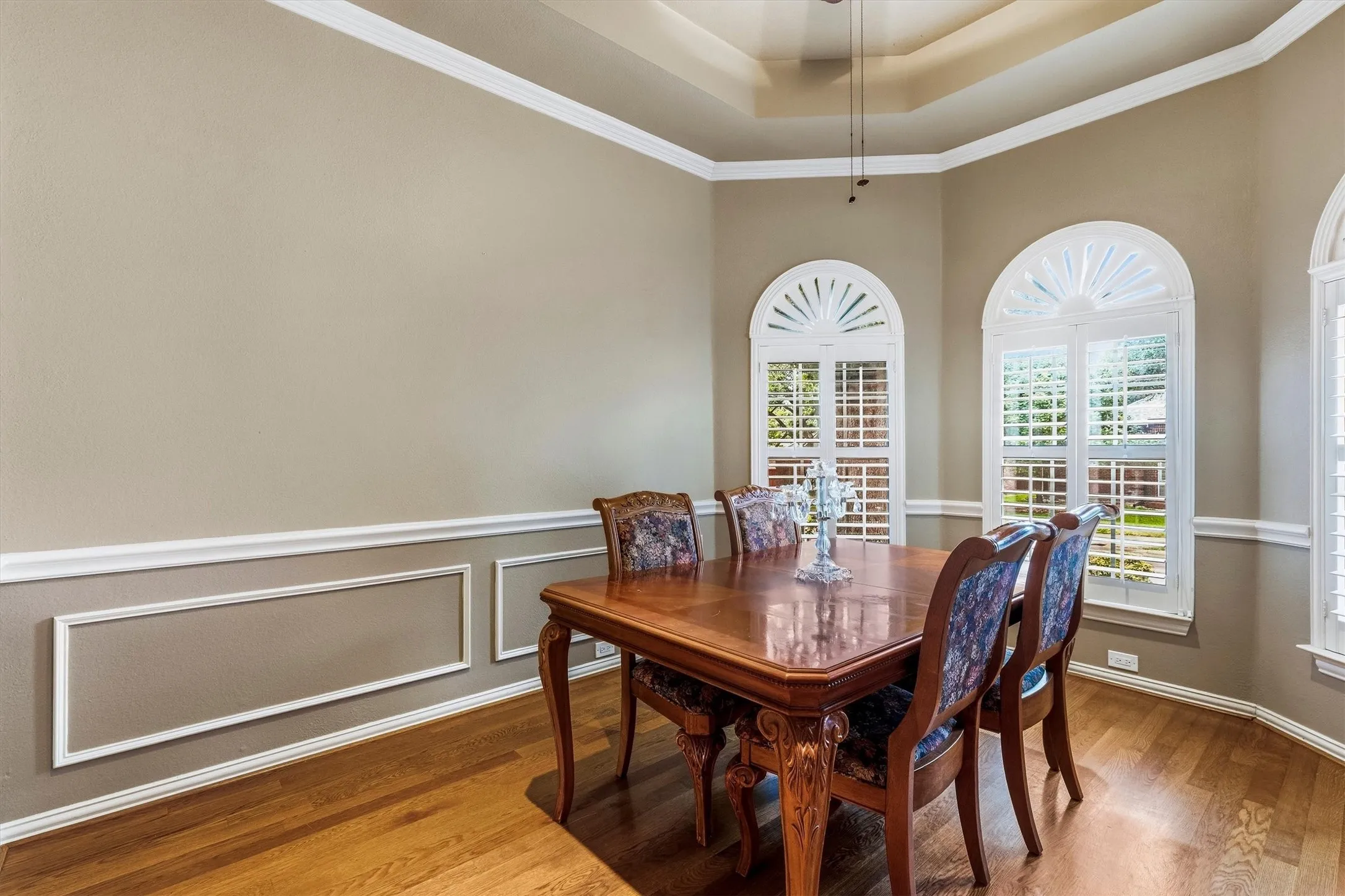 Tray ceiling, arched windows with plantation shutters, crown molding, chair rail with picture frame molding, and wood-finish flooring