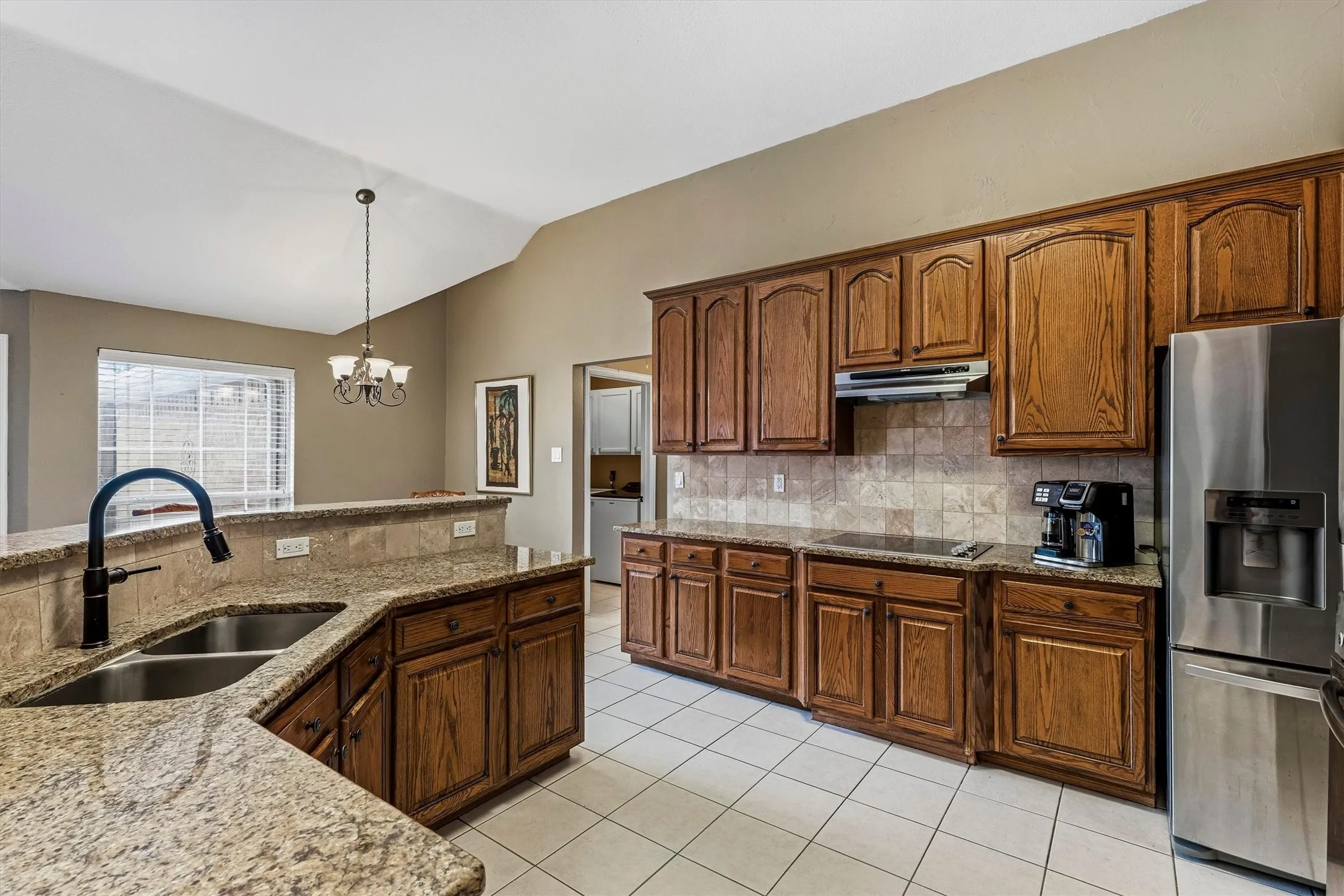 Kitchen featuring wood cabinetry, granite countertops, a double basin sink with a black fixture, stainless steel appliances, and tile flooring