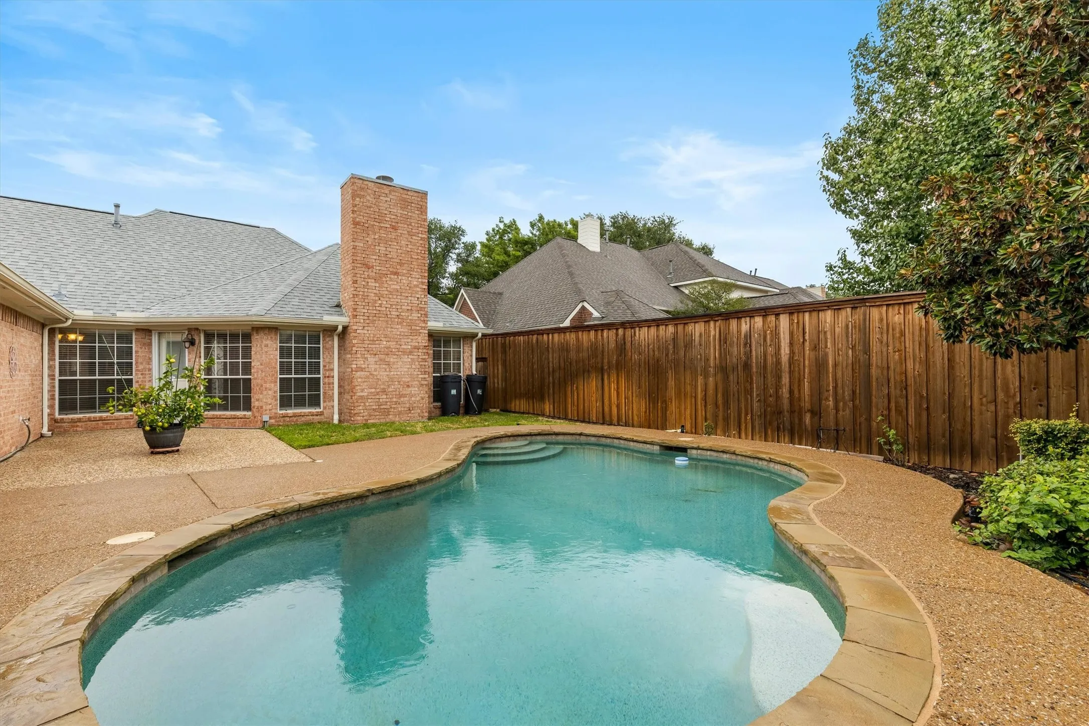 Backyard oasis featuring a free-form swimming pool, stone coping, and an expansive concrete patio