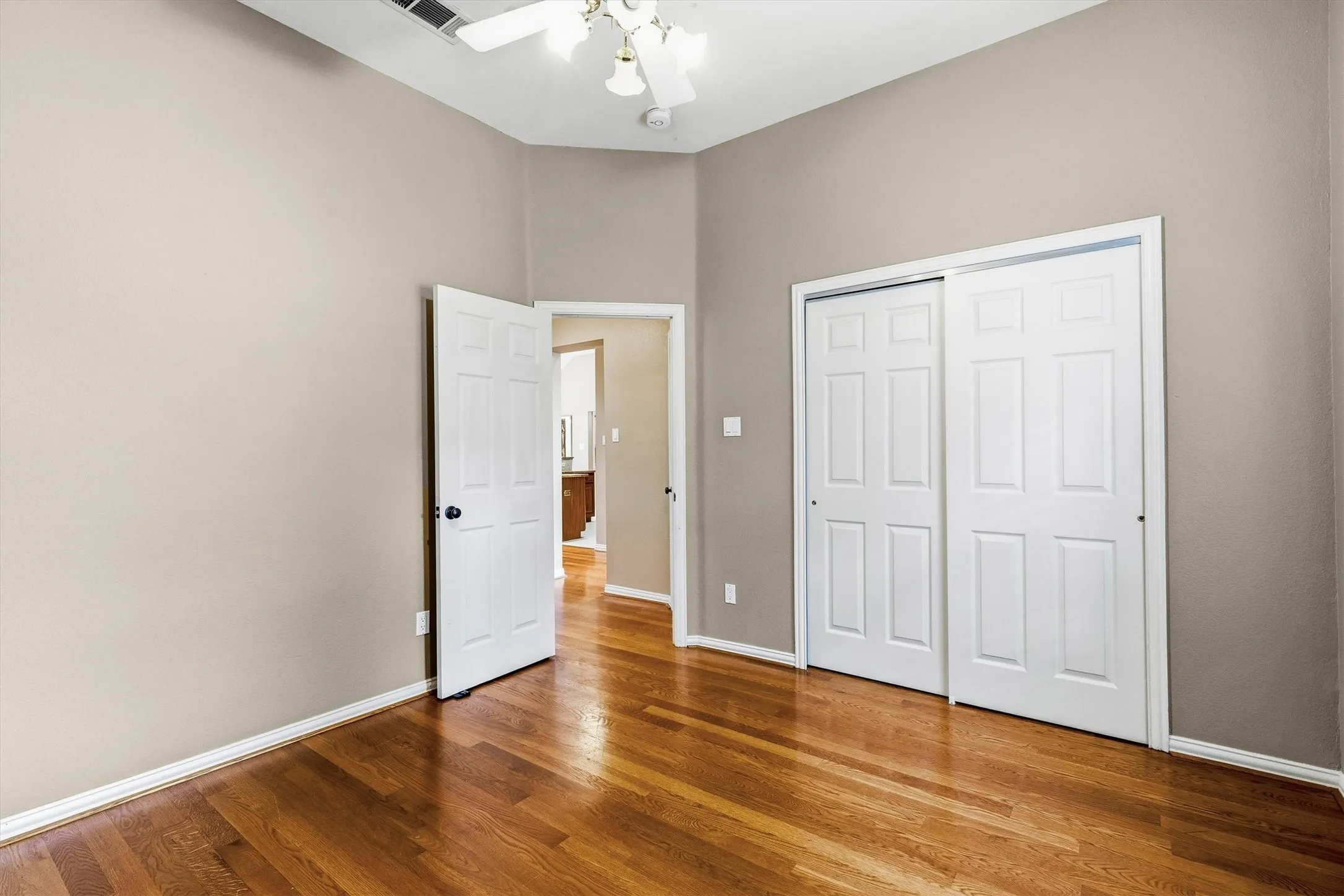 Vaulted ceiling, ceiling fan with light fixture, wood-finish flooring, two-panel sliding closet doors, and a paneled interior door