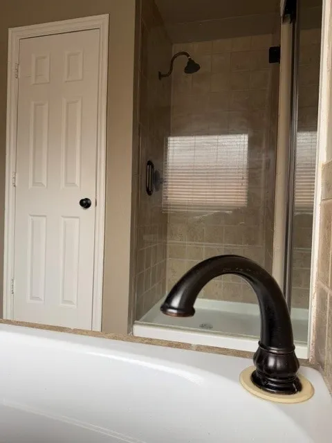 Tub with oil-rubbed bronze faucet and a tiled shower with glass enclosure