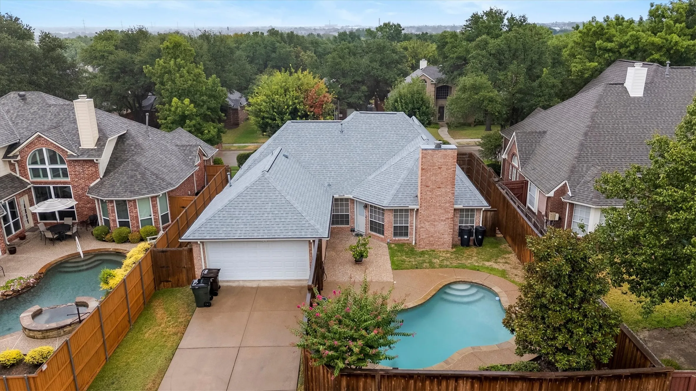 Elegant brick residence featuring a light-colored tile roof, expansive driveway with concrete paving, and resort-style backyard with sparkling swimming pool and spa