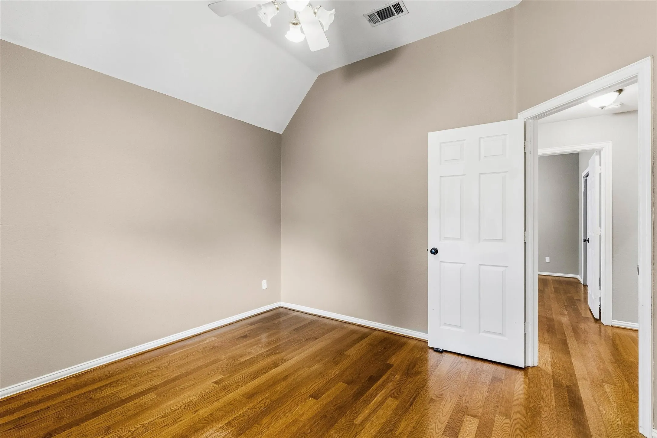 Vaulted ceiling with a ceiling fan, wood-finish flooring, and a paneled door with black hardware
