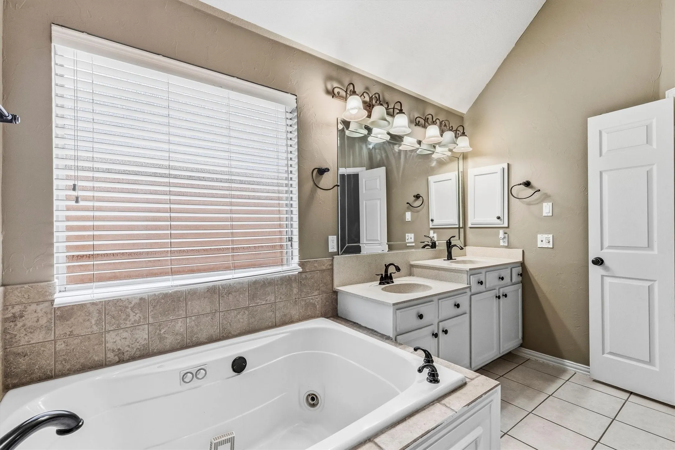 Jetted bathtub with tile surround, dual vanities with integrated sinks, and individual mirrors