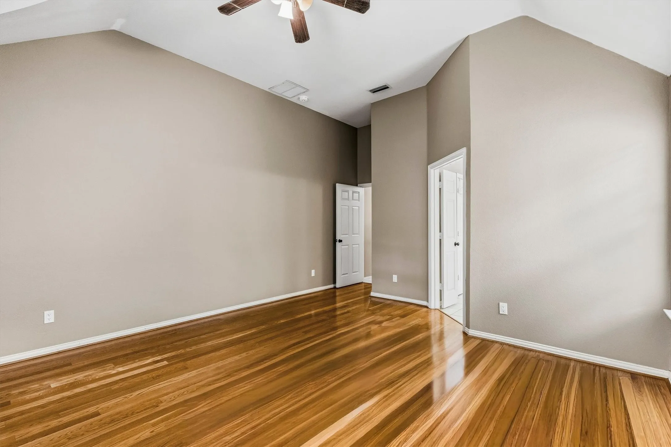 Vaulted ceiling with a ceiling fan, light wood-finish flooring, and neutral wall paint