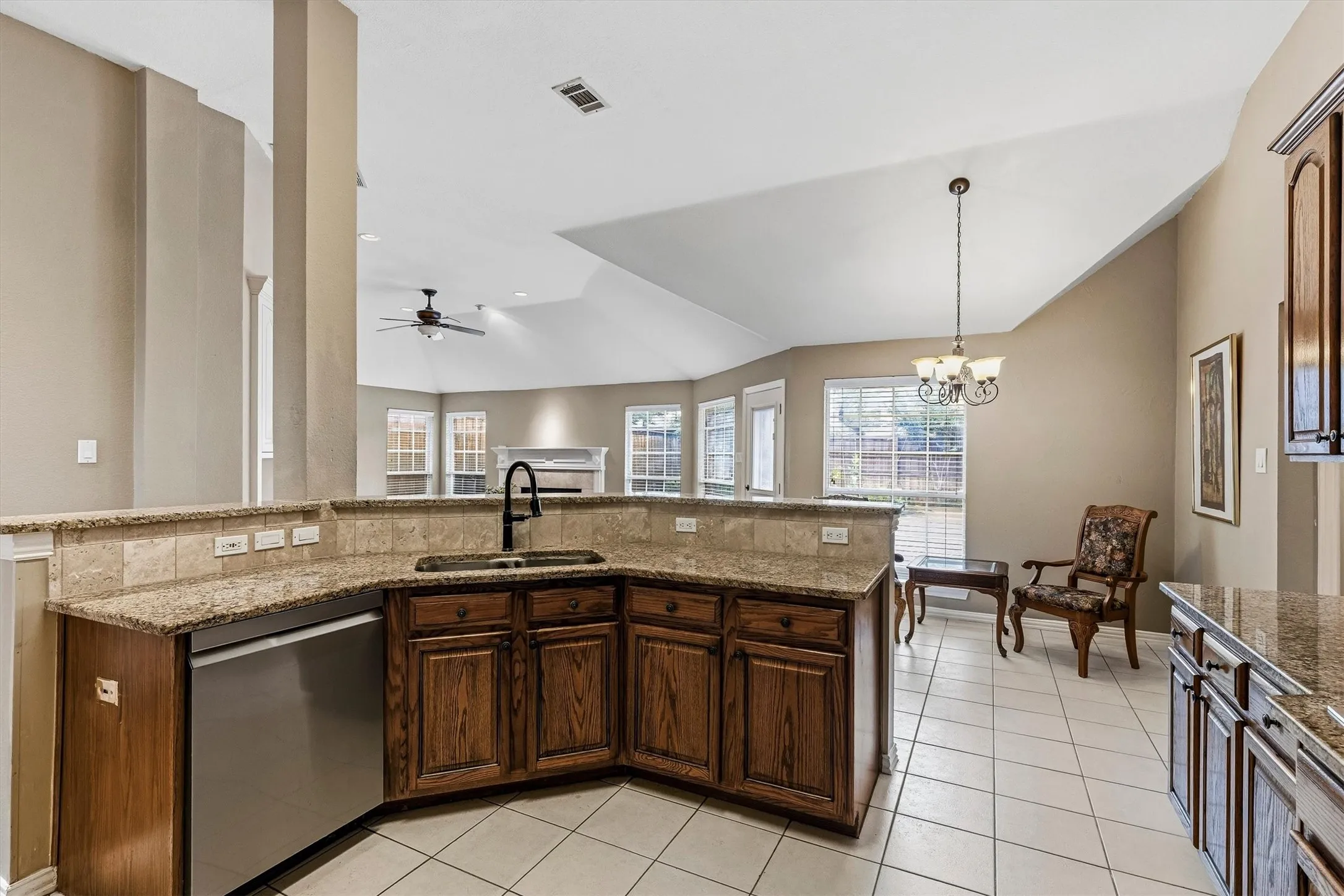 Kitchen featuring wood cabinetry, stainless steel dishwasher, a black gooseneck faucet, light granite countertops, and tile flooring