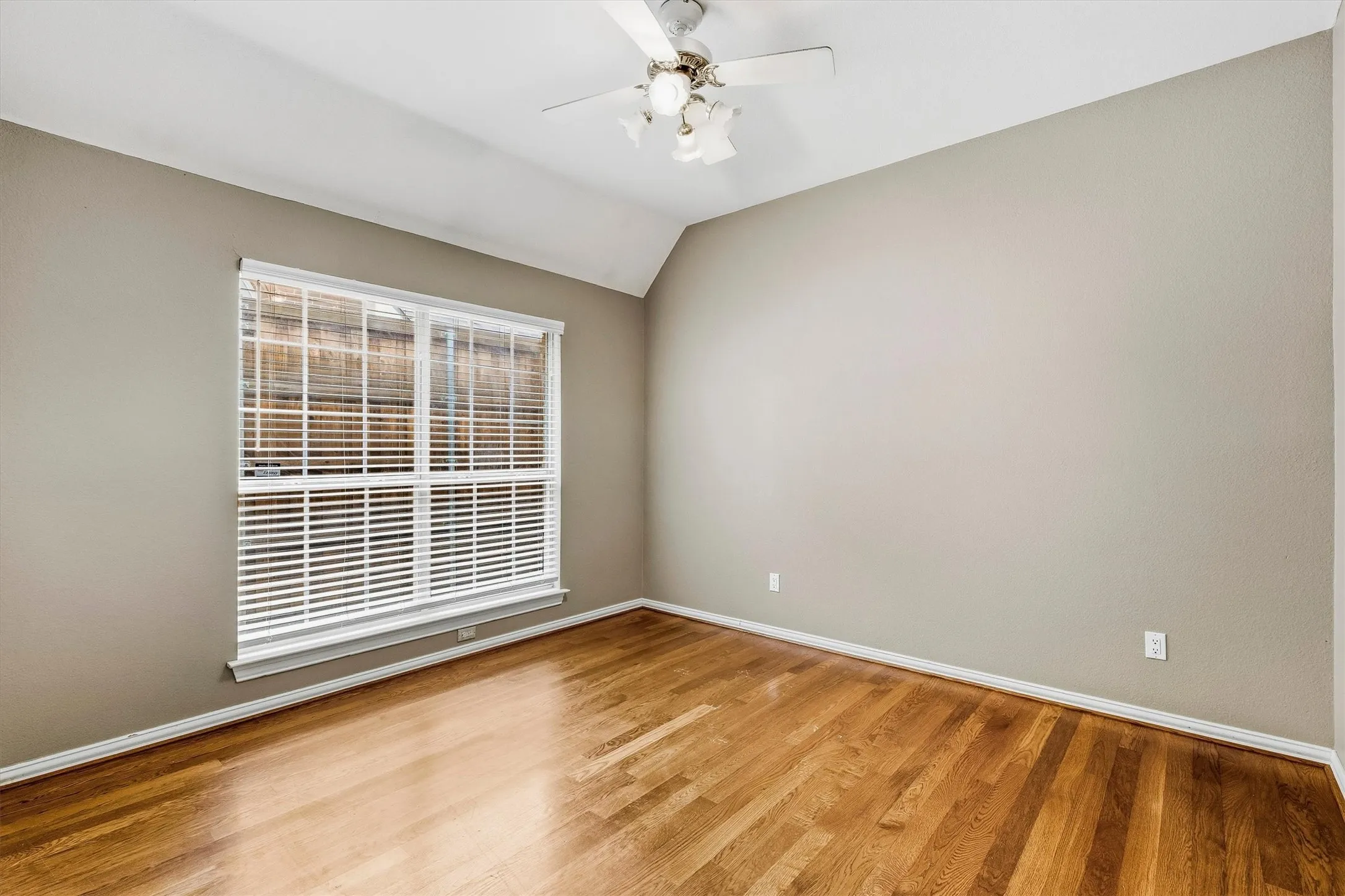 Vaulted ceiling with a ceiling fan, light neutral wall paint, wood-finish flooring, and a large window with white blinds