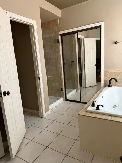 Soaking tub with black fixtures, tiled shower with glass enclosure, and white square tile flooring