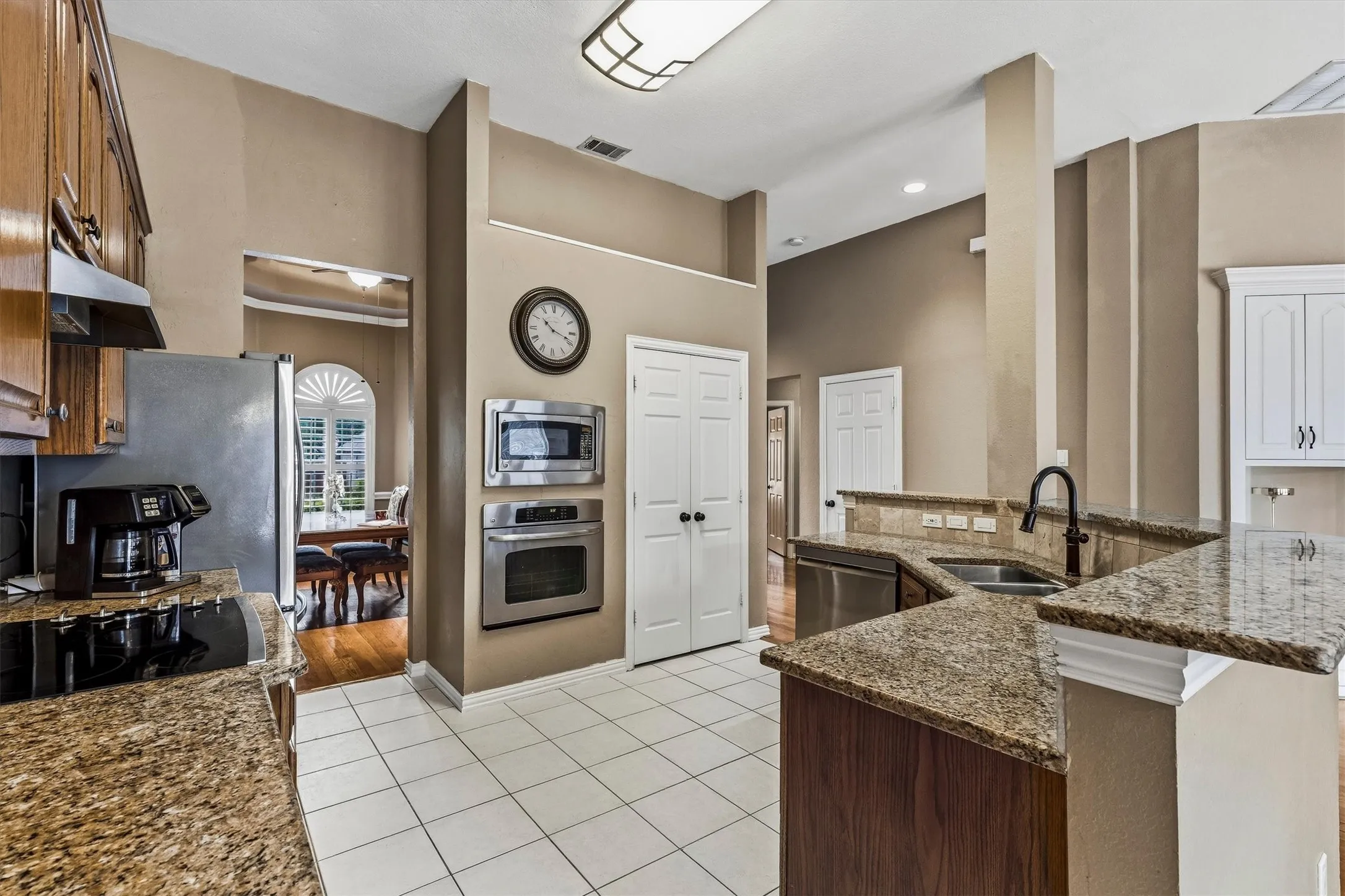Stainless steel appliances, built-in microwave, wall oven, granite countertops, and white tile flooring