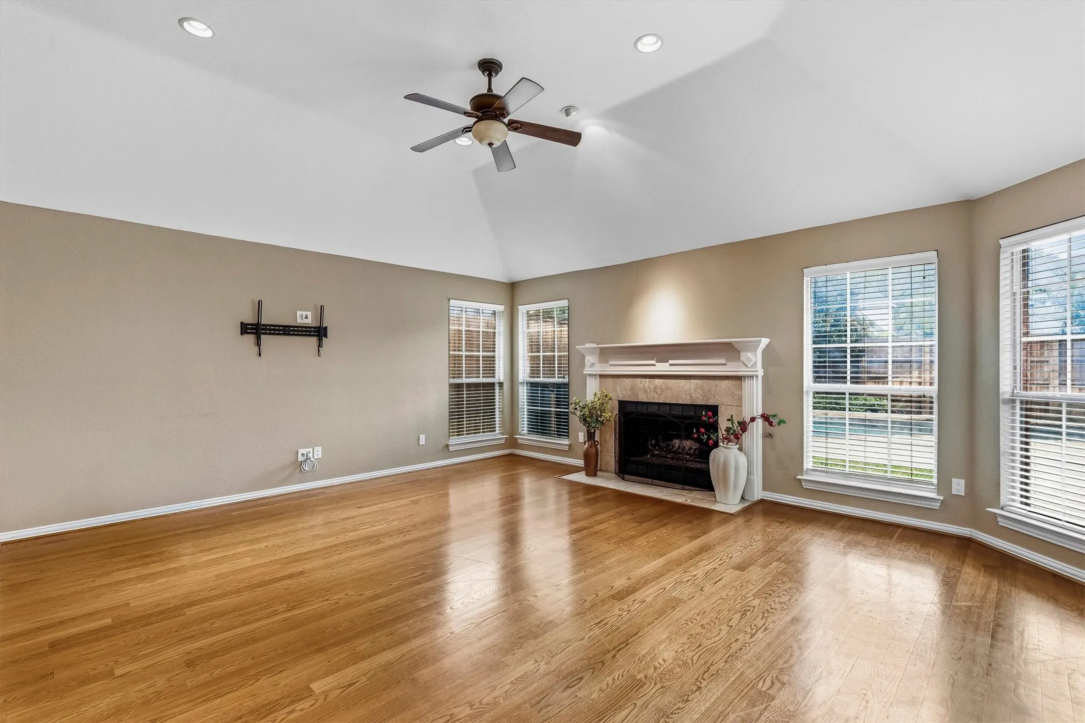 Spacious living area featuring gleaming wood-finish flooring, vaulted ceilings with recessed lighting, and a ceiling fan