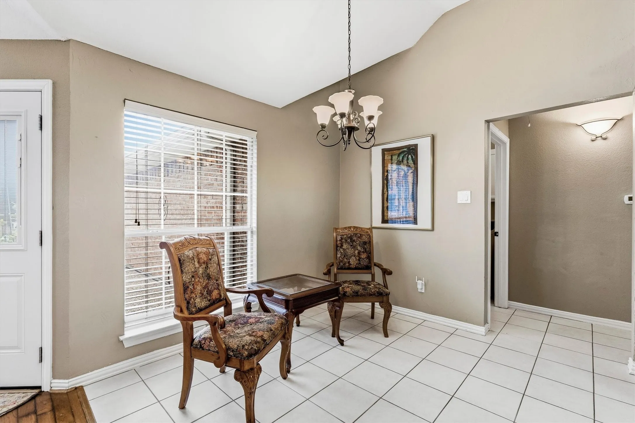 Vaulted ceiling, white tile flooring, large window with blinds, wall sconce lighting, and a chandelier