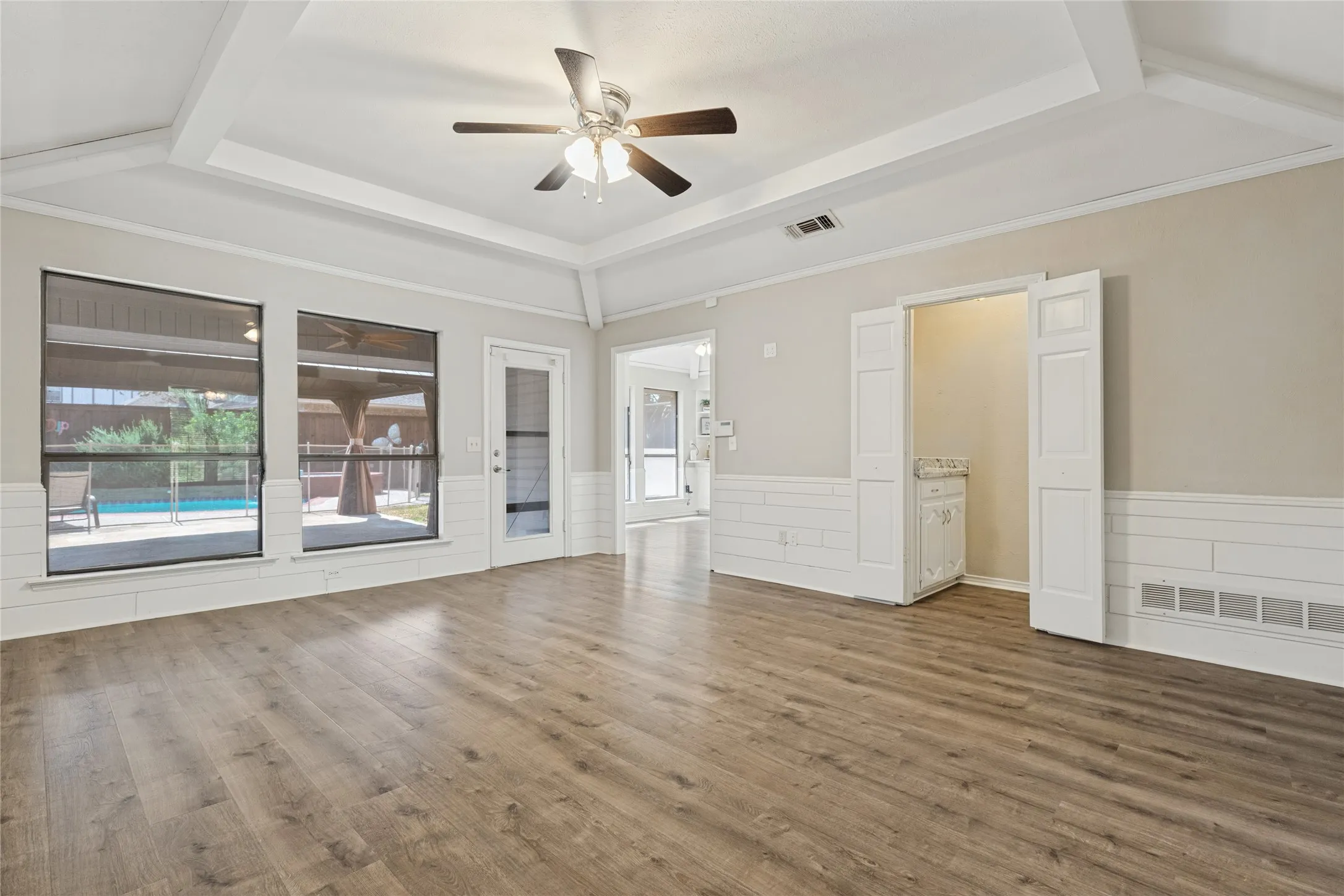 Wood-finish flooring, white shiplap wainscoting, a tray ceiling with a ceiling fan, and large windows with outdoor access to the cabana and pool view.   Dry bar with tiffany light fixture.