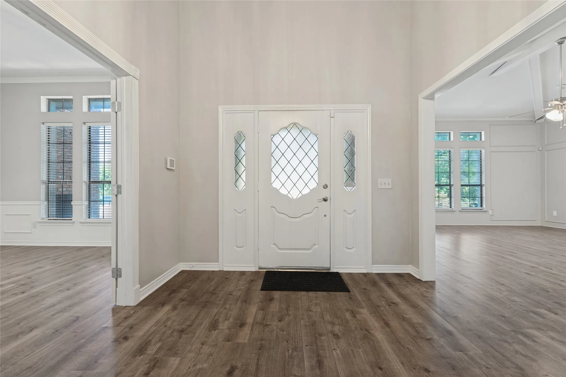 Entryway featuring wood-finish flooring, a white front door with leaded  glass inserts, and high ceilings