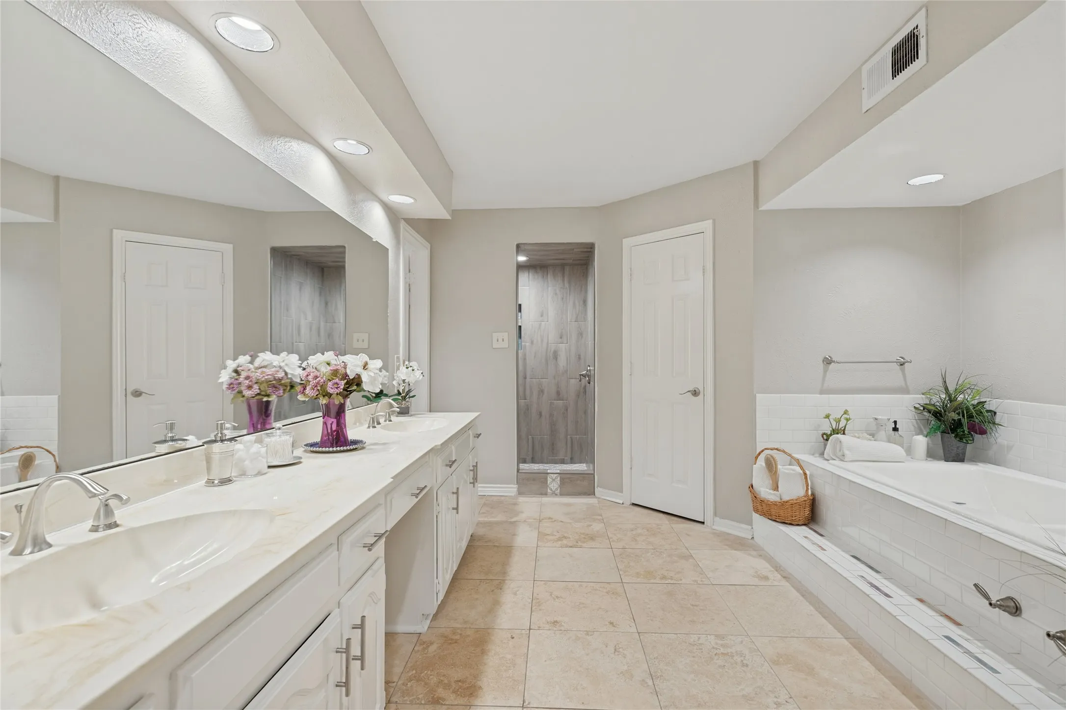 Dual vanity with integrated sinks and extensive countertop space, cabinet storage, vanity area, two separate walk in closets, recessed lighting, built-in bathtub with subway tile surround, and a walk-in shower with custom porcelain tile design, travertine tile flooring