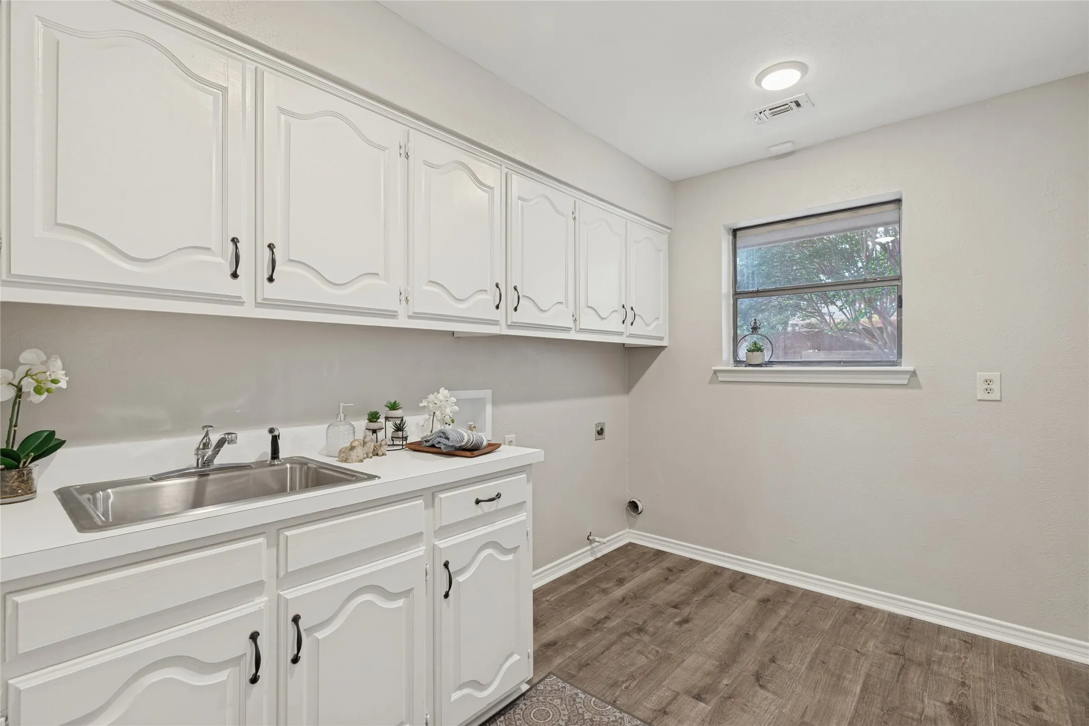 White cabinetry with dark hardware, stainless steel sink, countertop, wood-finish flooring, and recessed lighting, fresh and airy, with plenty of room for a freezer or second refrigerator
