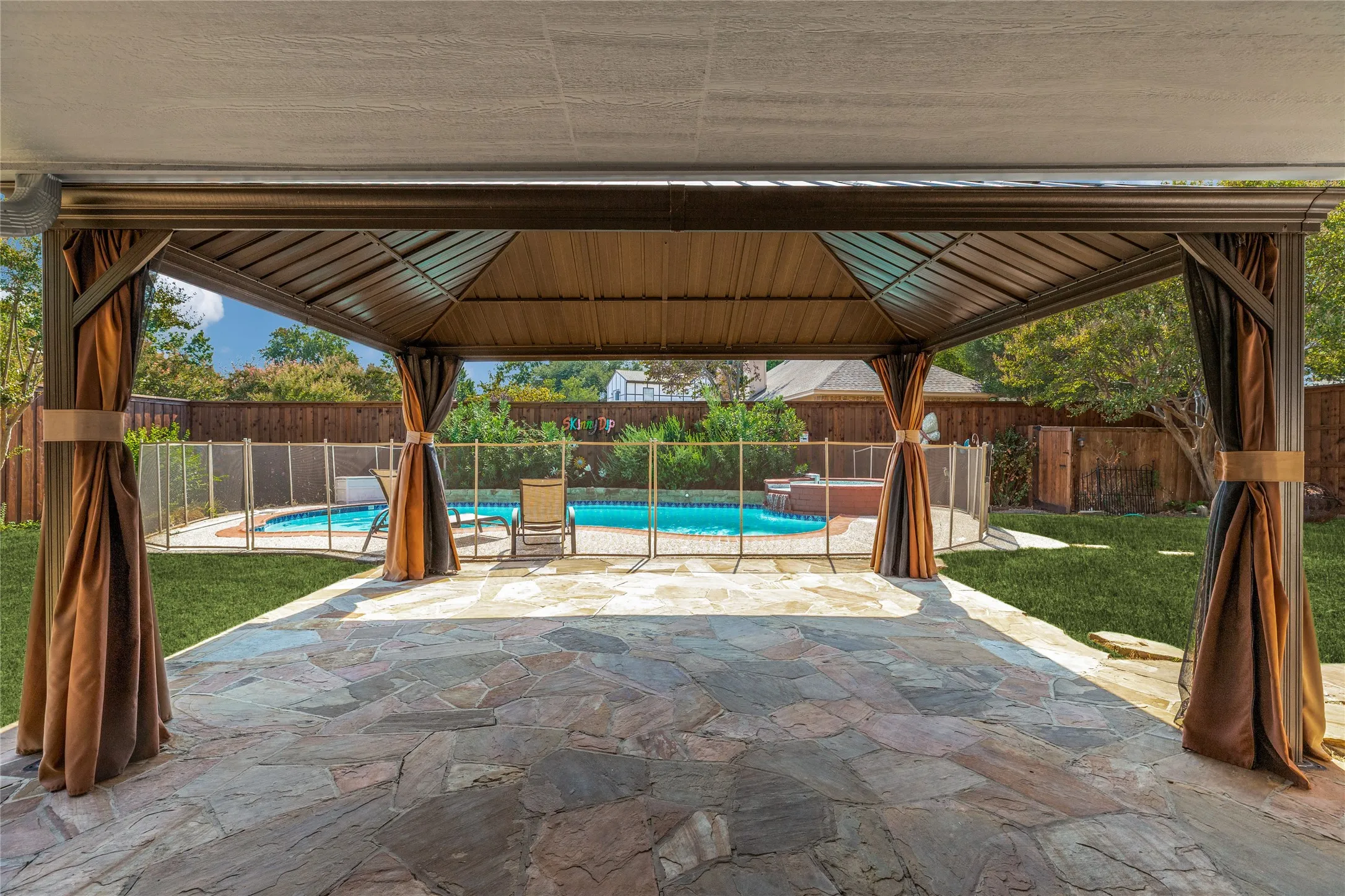 Expansive flagstone patio with a covered gazebo featuring privacy curtains, poolside