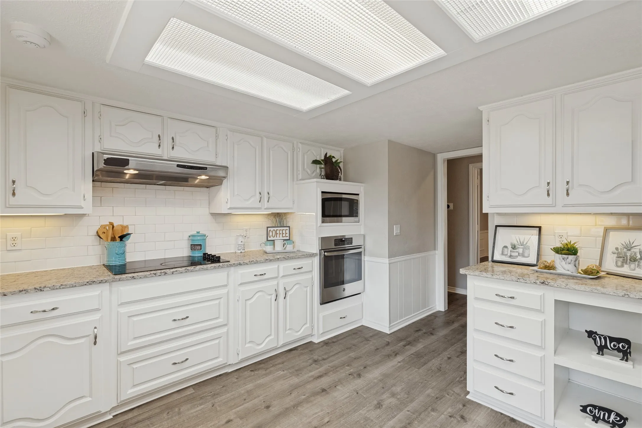 White cabinetry with decorative hardware, granite countertops, stainless steel appliances, and wood-finish flooring