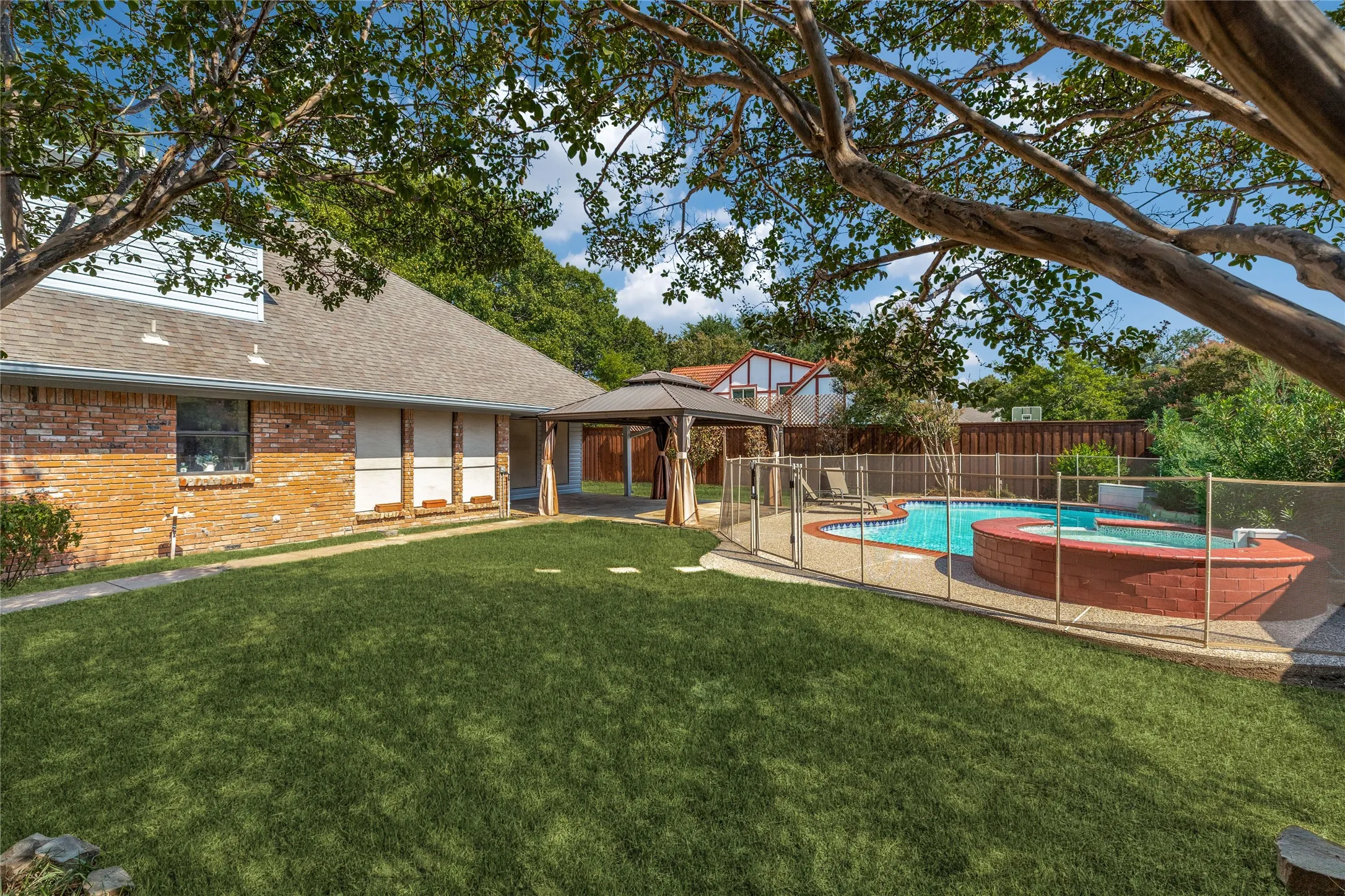 Expansive lawn area with a fenced swimming pool, integrated spa, and an outdoor gazebo