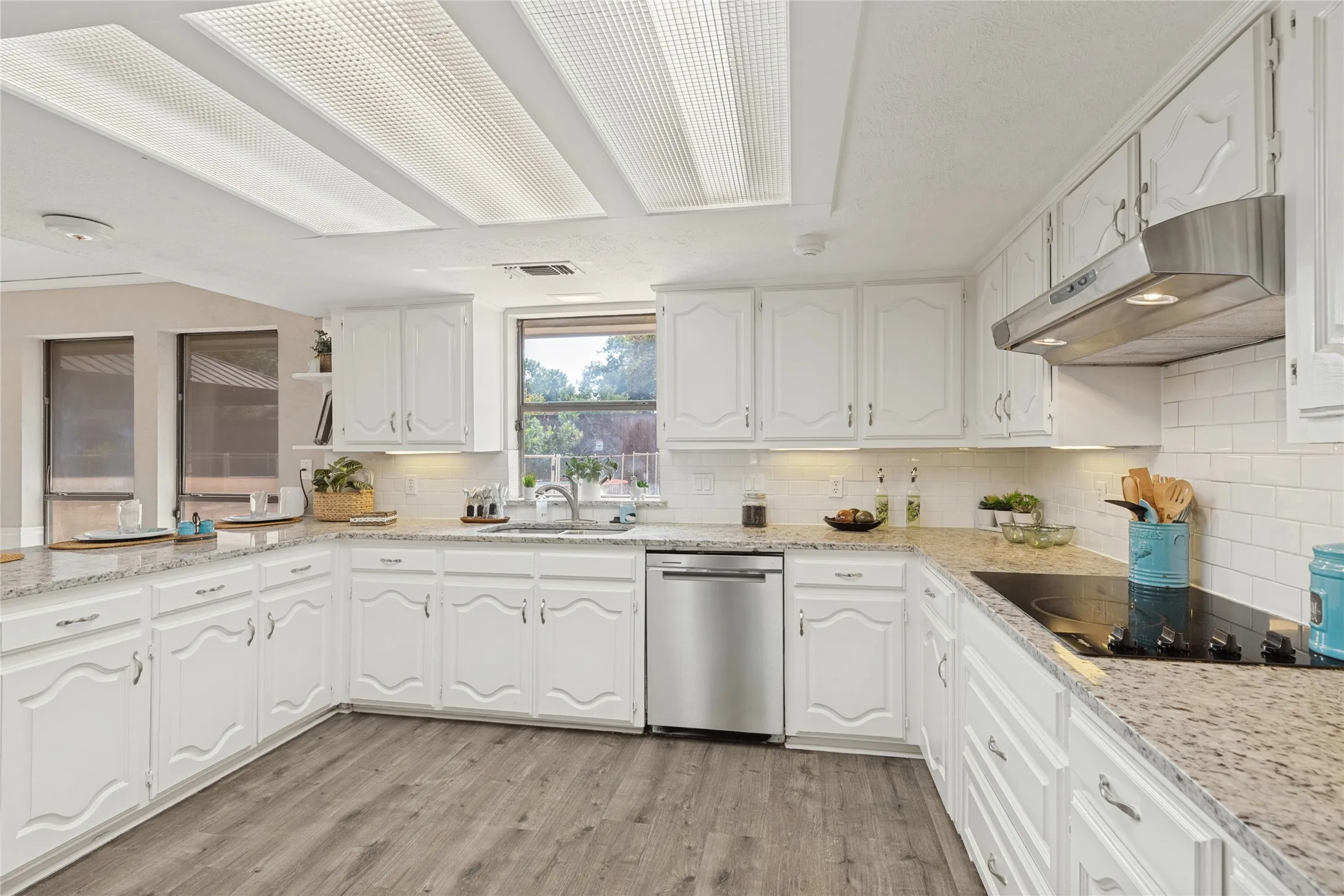White cabinetry, granite countertops, subway tile backsplash, stainless steel dishwasher, and a built-in cooktop