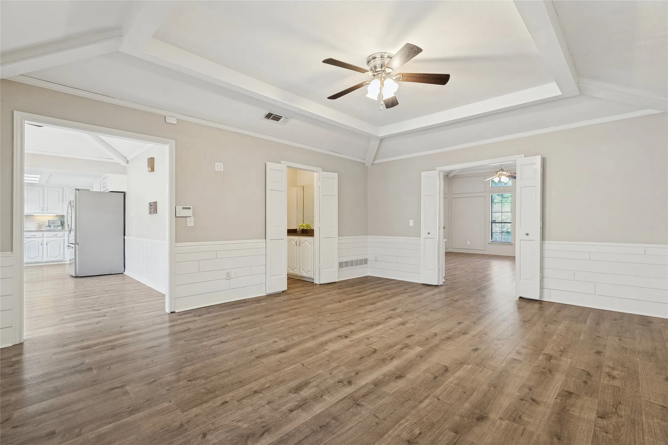 Wood-finish flooring, tray ceiling with recessed lighting, ceiling fan, shiplap wall accent, and bi-fold doors