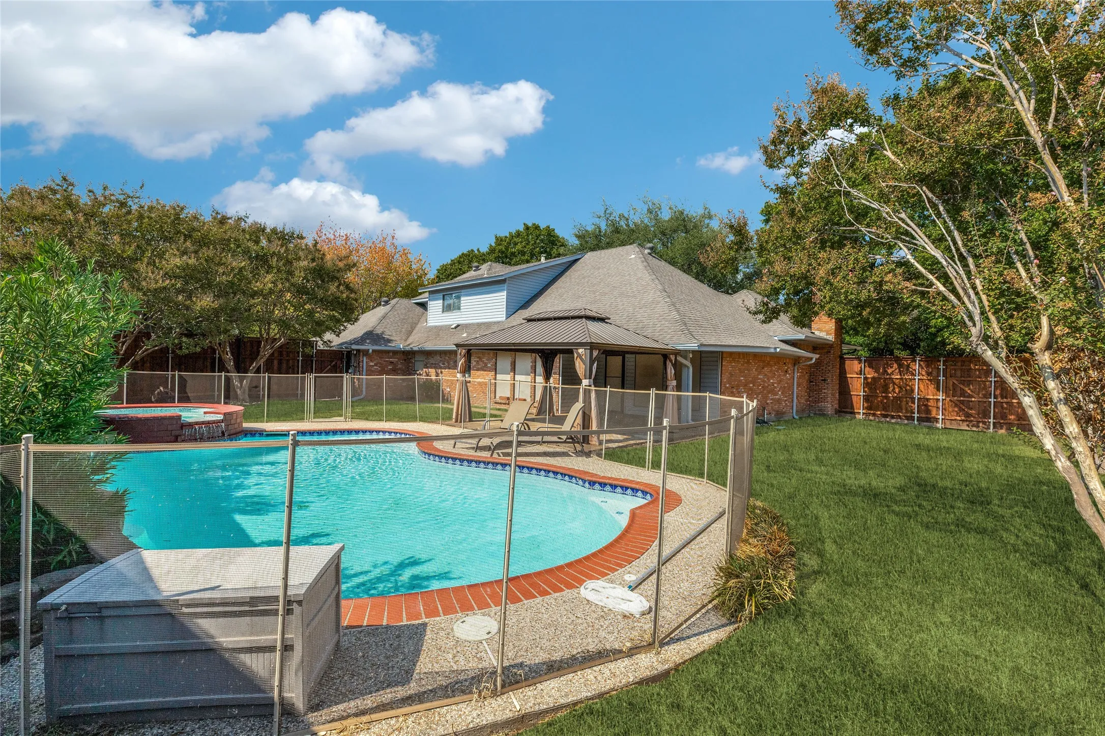 Backyard featuring a freeform swimming pool, integrated spa, surrounding stone aggregate decking, and a privacy fence