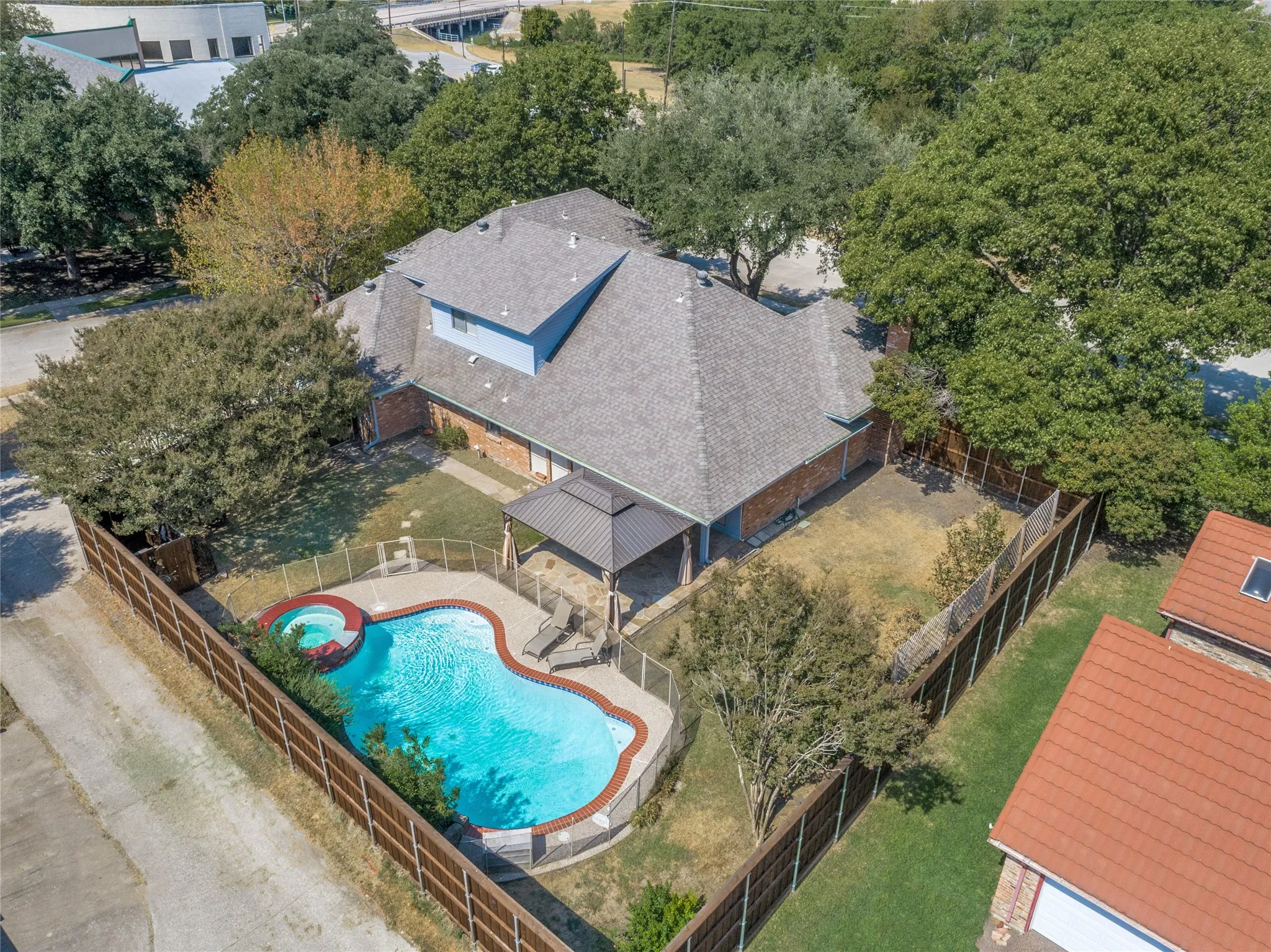 Aerial view showcasing a custom-shaped resort-style swimming pool with integrated spa, surrounded by mature landscaping and wooden fencing