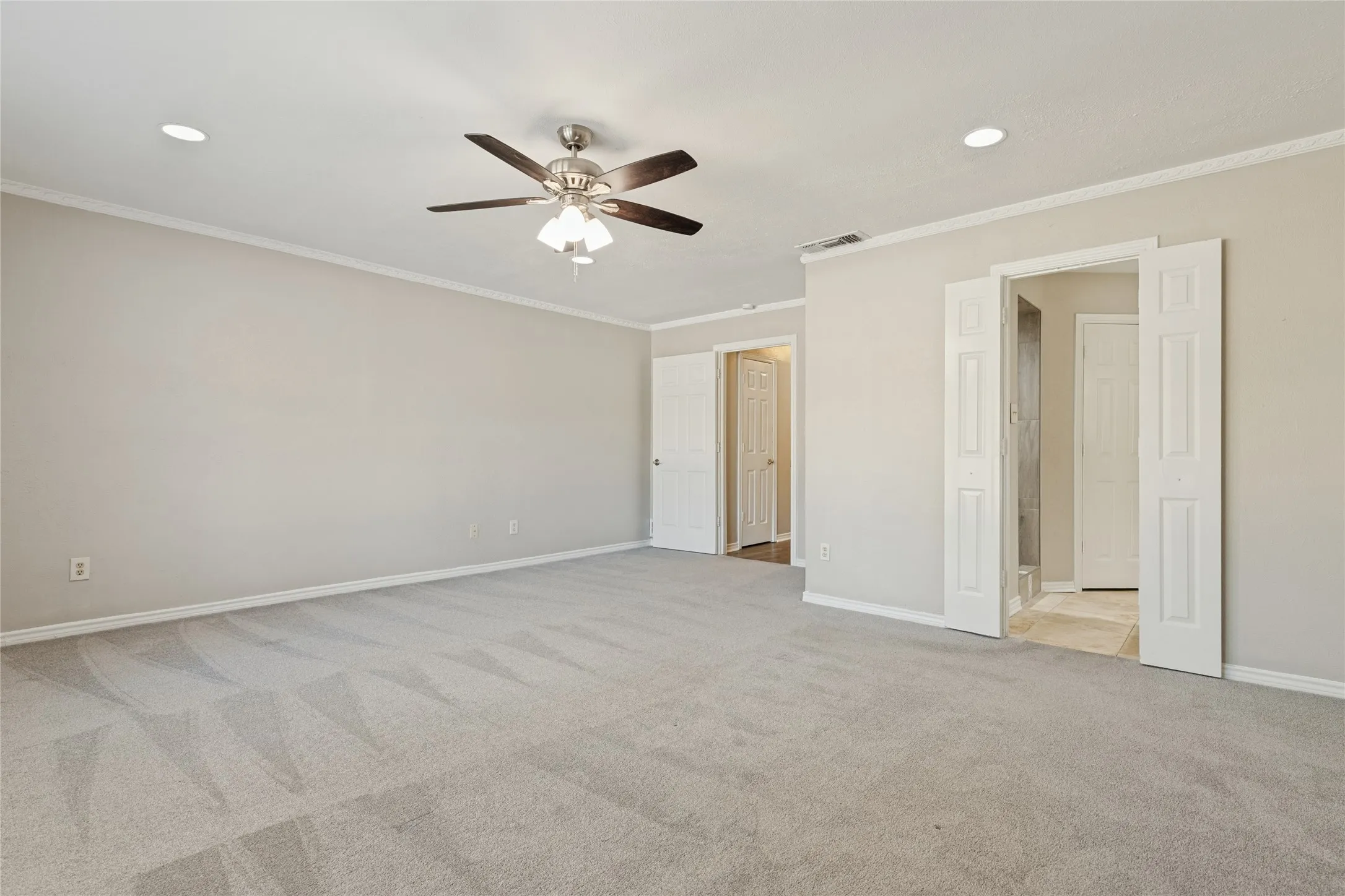 Spacious primary bedroom featuring neutral carpet, recessed lighting, a ceiling fan, and crown molding, large windows, and an ensuite bath