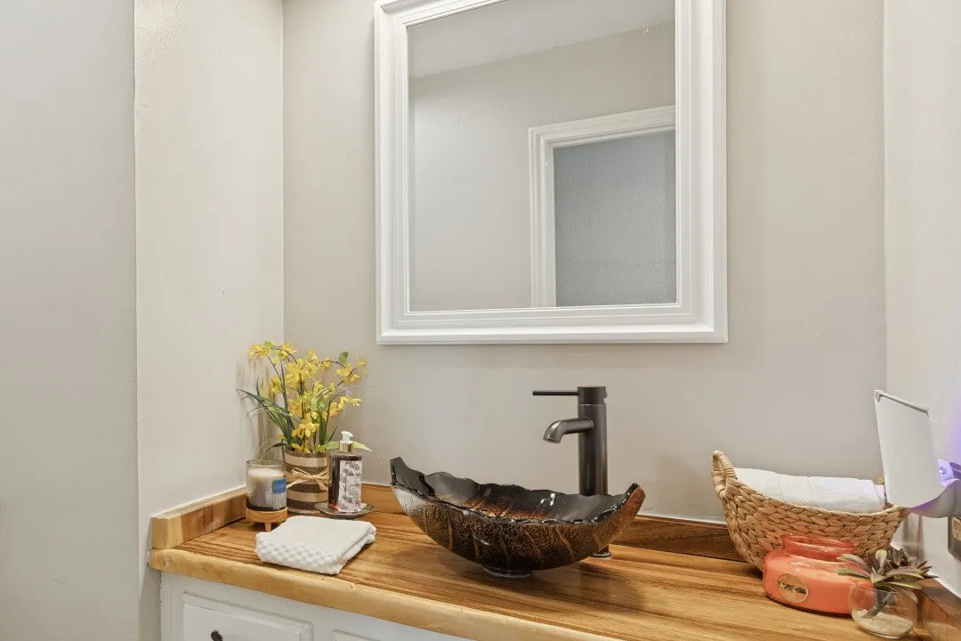 Wood-finish countertop with a vessel sink, dark bronze faucet, and a framed wall mirror