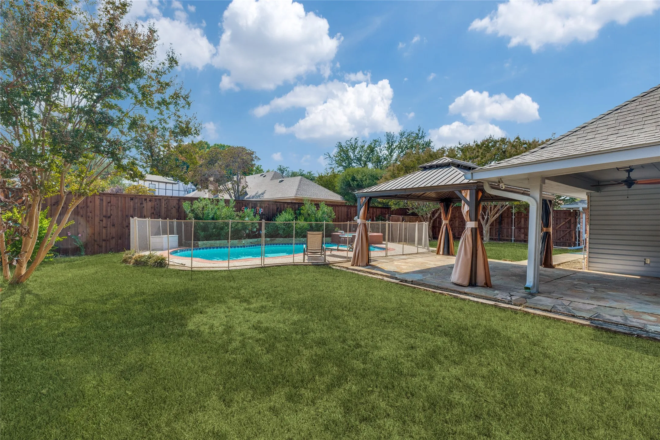 Expansive backyard featuring a fenced swimming pool, dedicated patio area, gazebo with privacy curtains, and a covered outdoor living space, cedar privacy fence with gates
