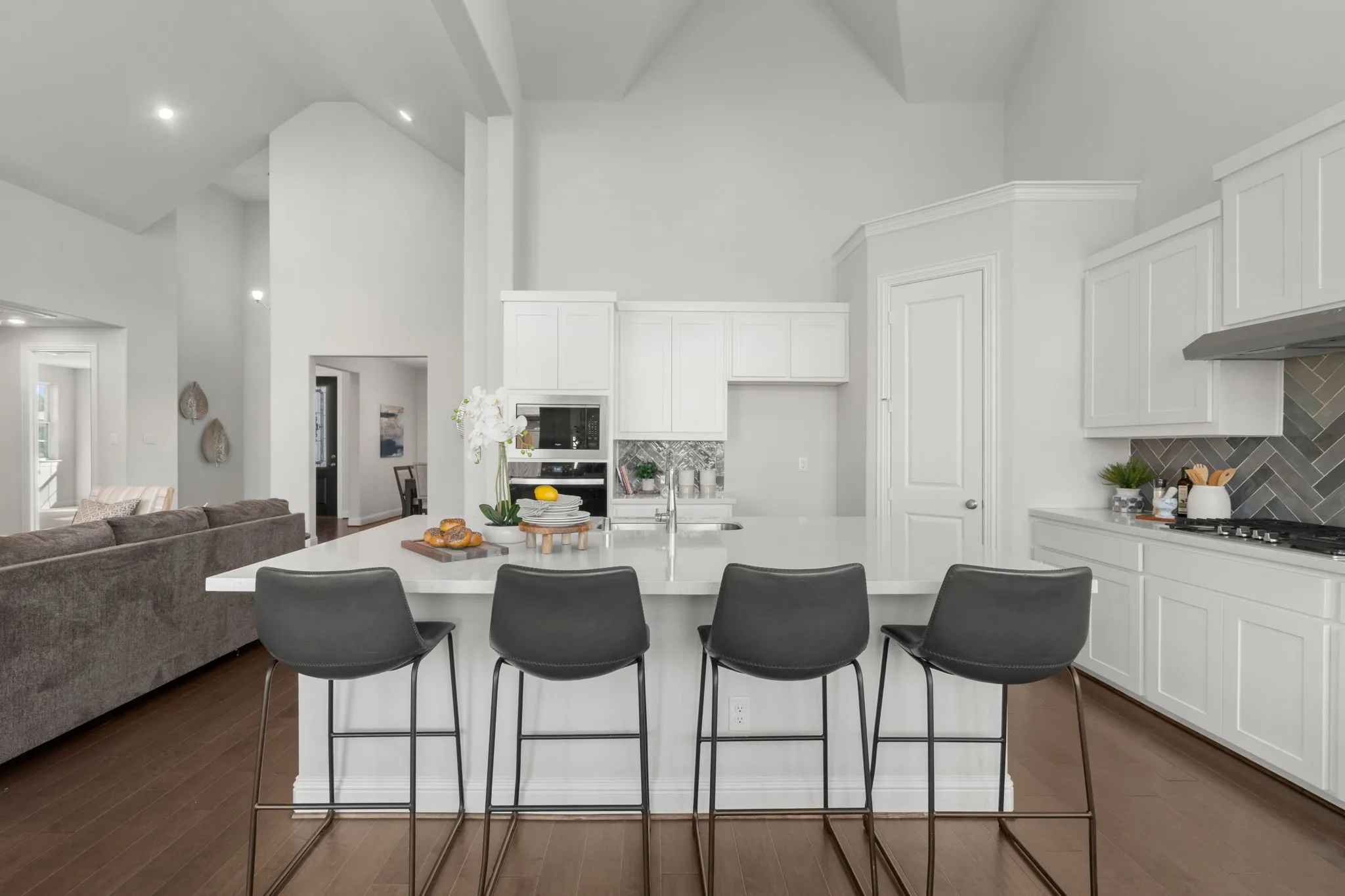White shaker cabinetry, herringbone tile backsplash, stainless steel appliances, central island with seating, and wood-finish flooring