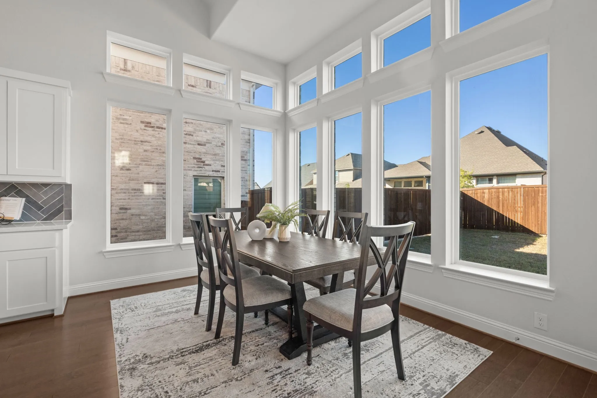 Expansive window array, rich wood-finish flooring, white shaker cabinetry, herringbone tile backsplash, light-toned walls