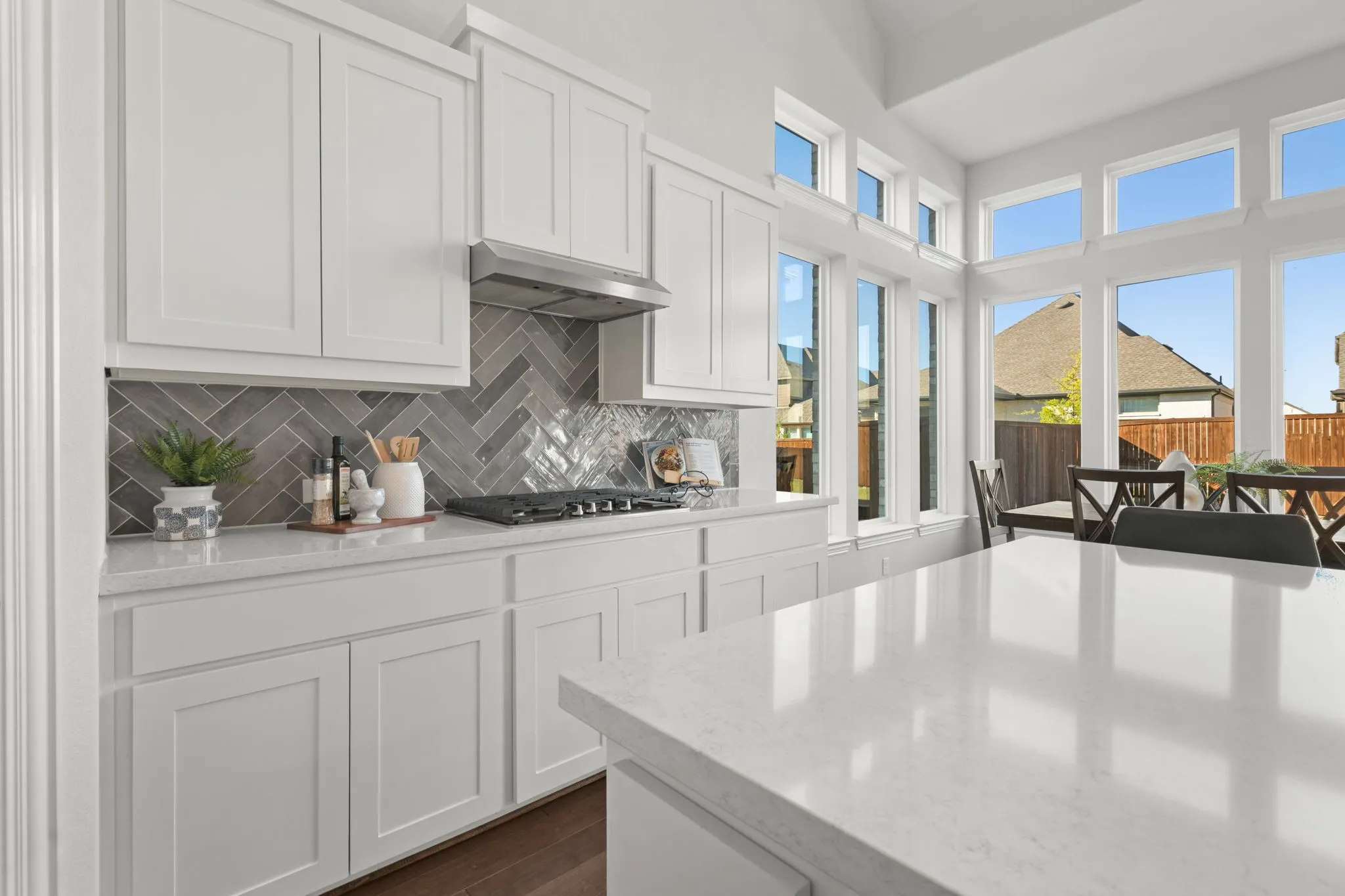 White shaker cabinetry with a herringbone tile backsplash and quartz island
