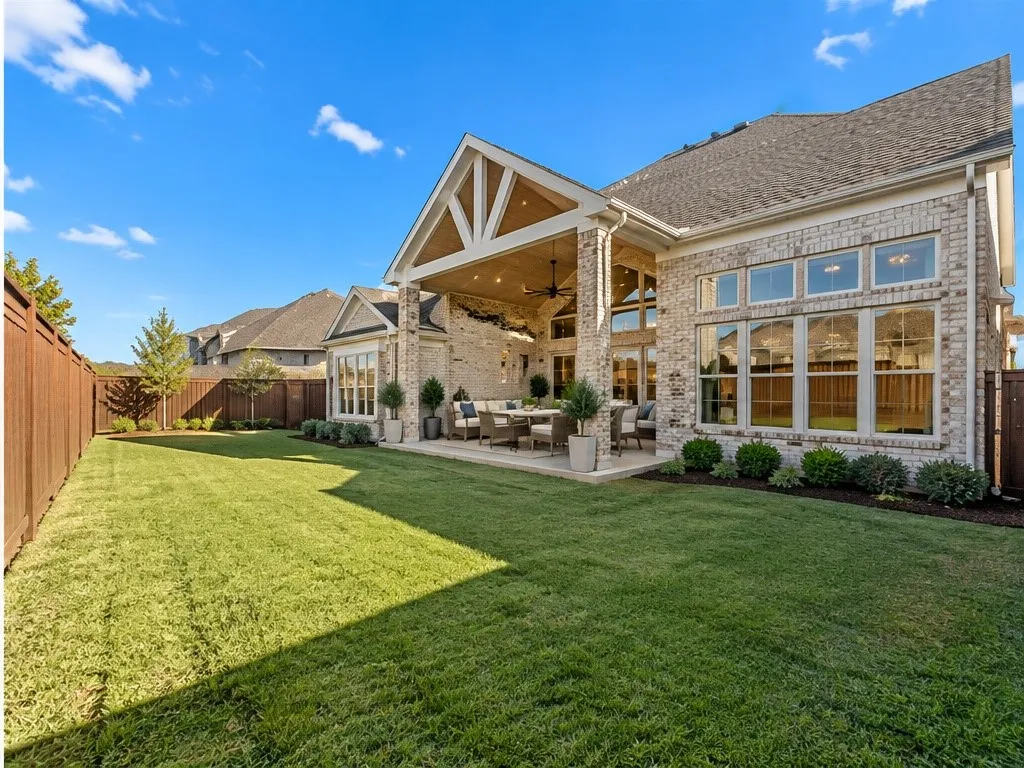 Expansive backyard with a covered patio, brick exterior, multiple large windows, and a wood privacy fence