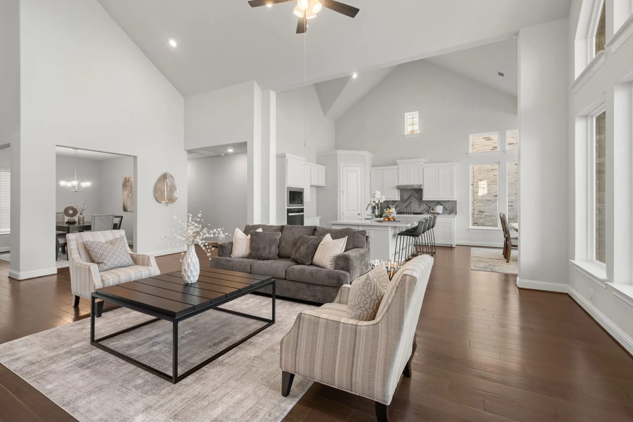 Soaring vaulted cathedral style ceilings, rich wood-finish flooring, abundant natural light, recessed lighting, and a kitchen featuring white cabinetry - Open Floor Plan