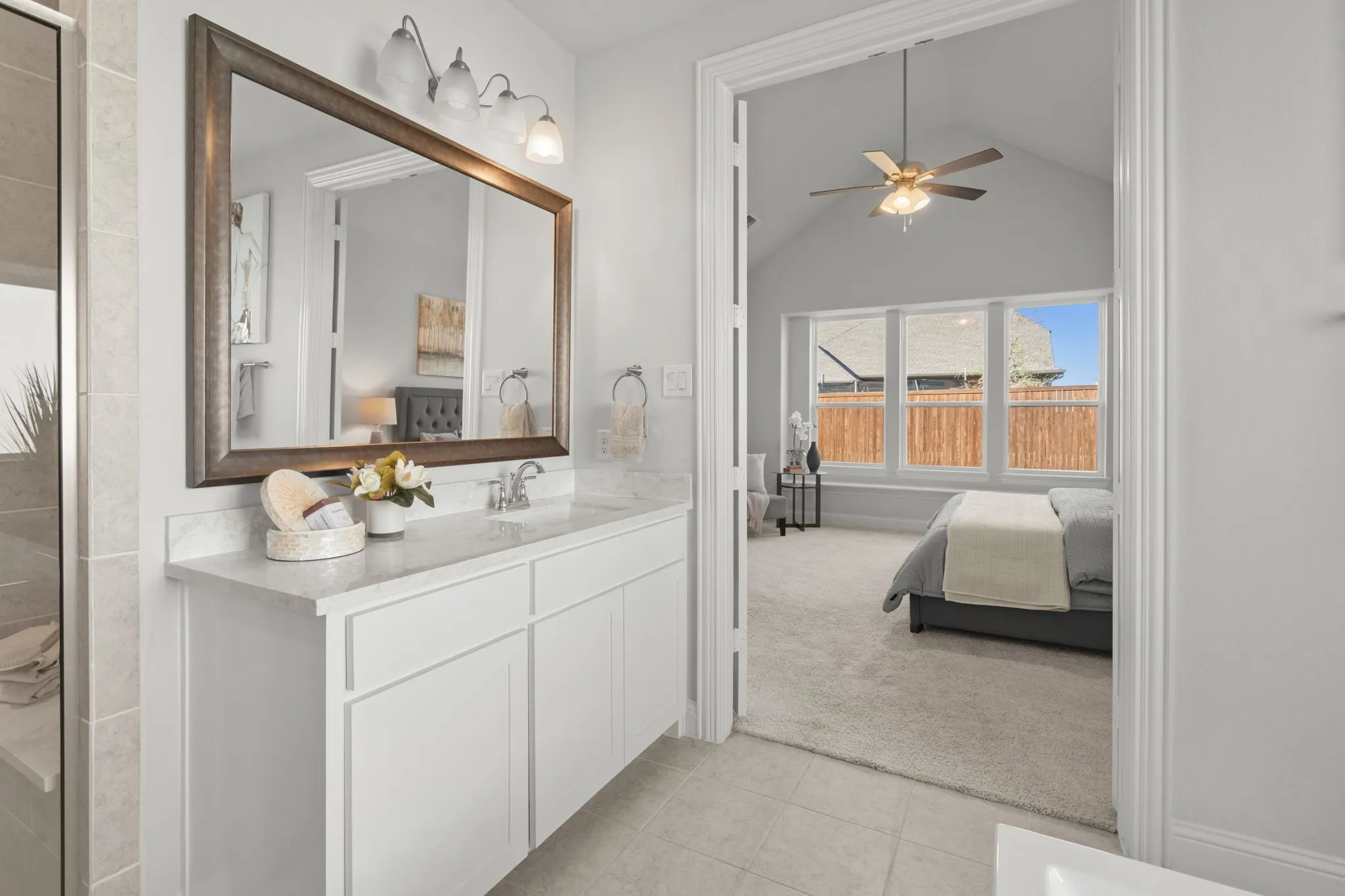 Primary bathroom featuring a white vanity with dual sink configuration, wood-framed mirror with integrated lighting, and tile flooring