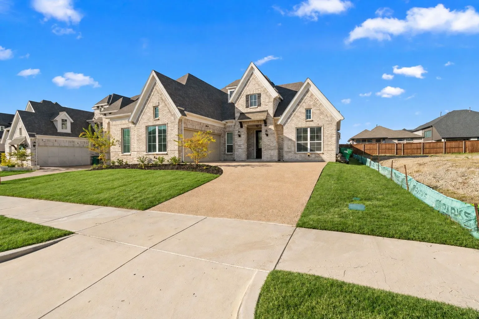 Stone exterior with multiple gables, large windows, an expansive driveway, and manicured landscaping