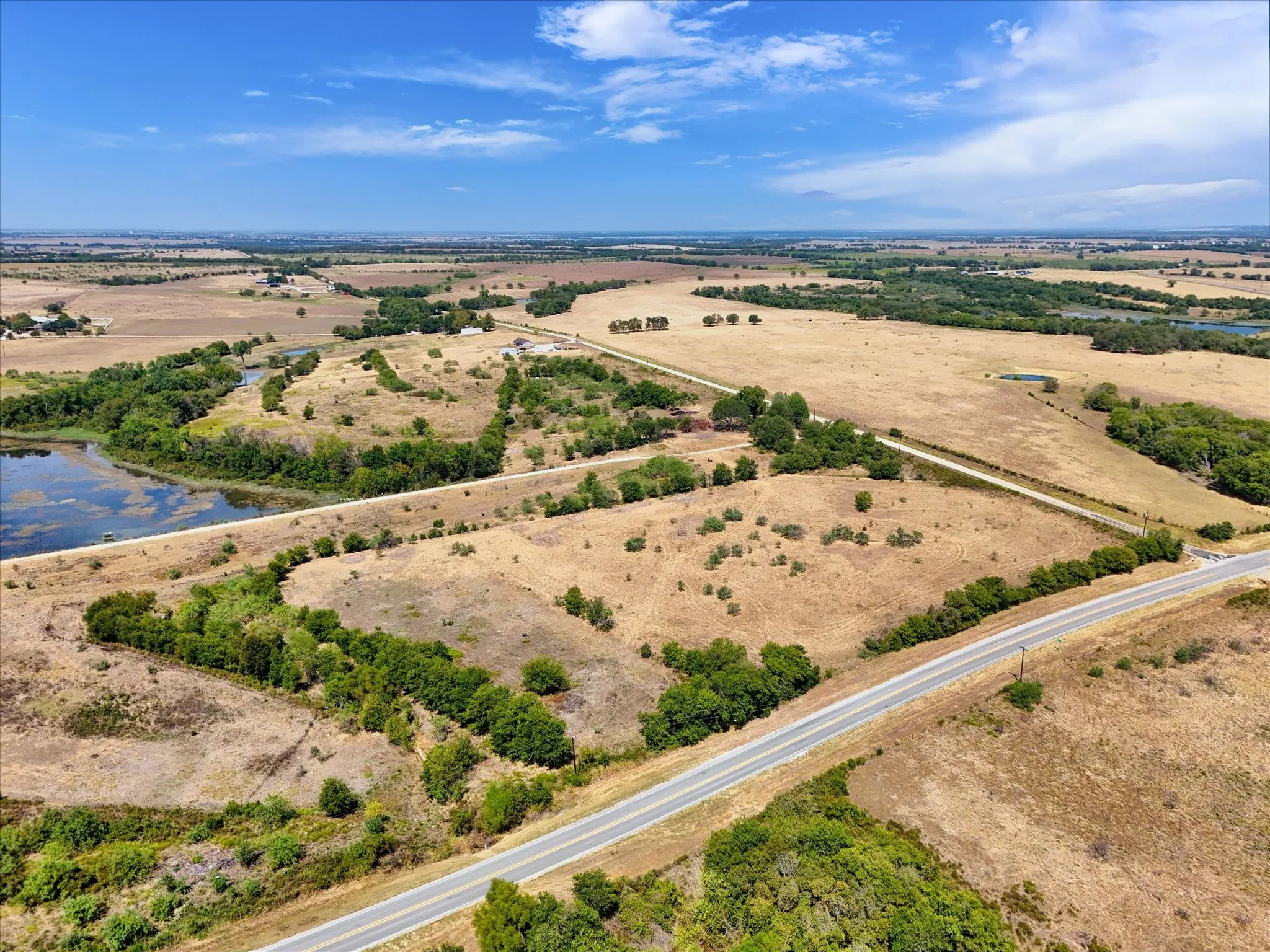 Expansive rural landscape featuring a paved road, natural water body, and scattered trees