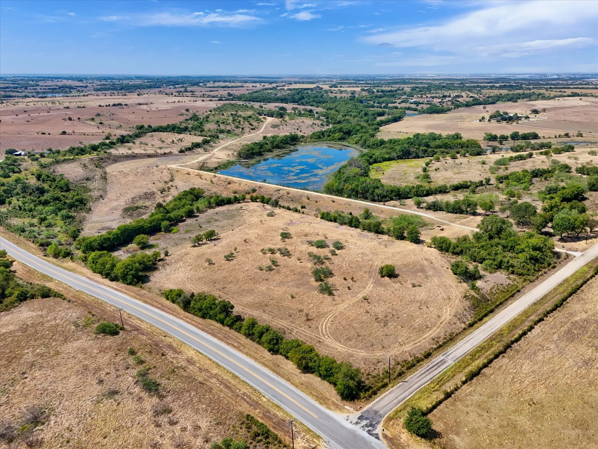 Expansive land featuring a natural pond, established trees, and paved road frontage