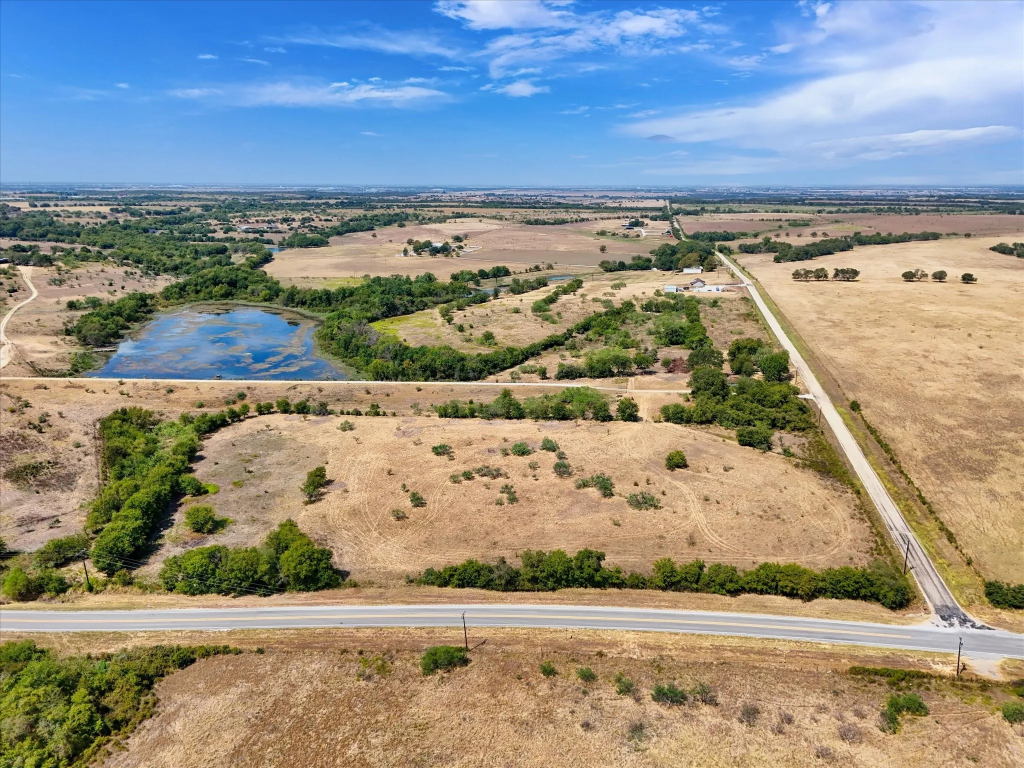 Expansive parcel featuring a natural pond, established tree lines, and open fields with a paved road frontage